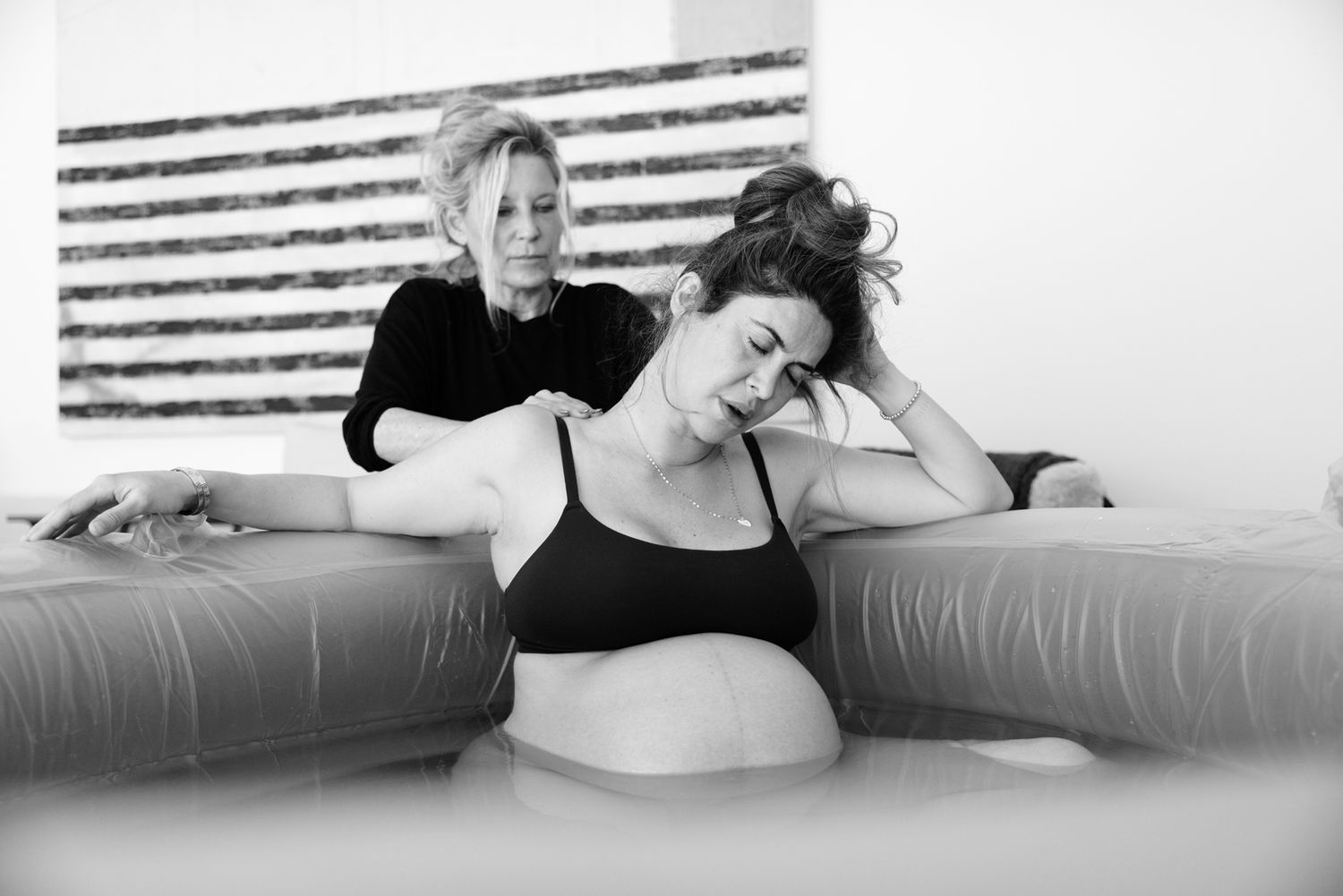 A midwife supports a laboring woman in an inflatable birthing pool.