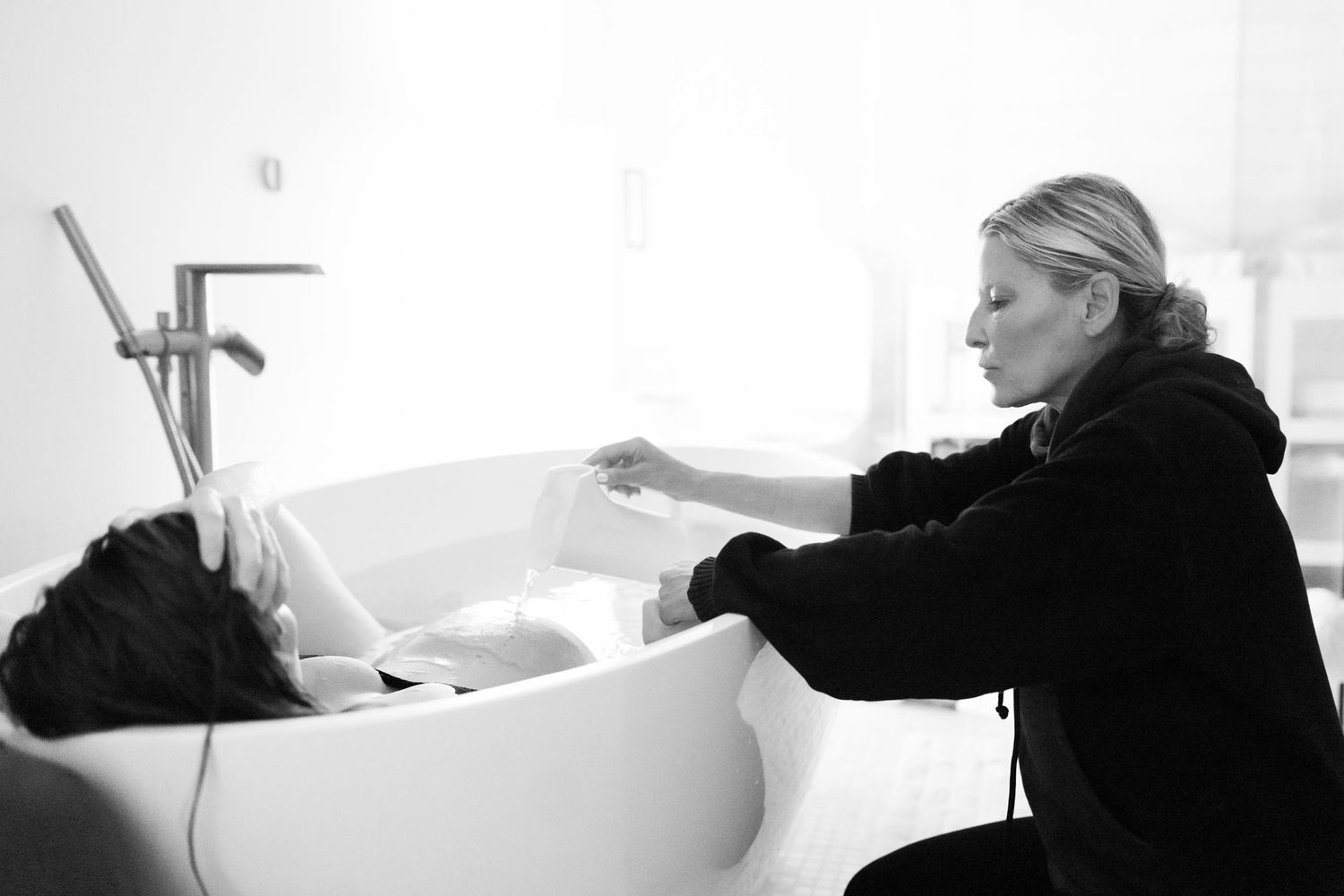 Midwife attending to woman during water birth in modern white bathroom.