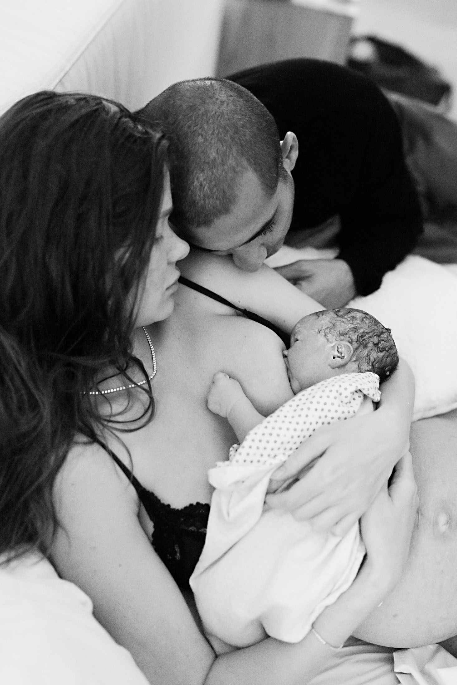 New parents share a kiss over their newborn baby held in mothers arms.