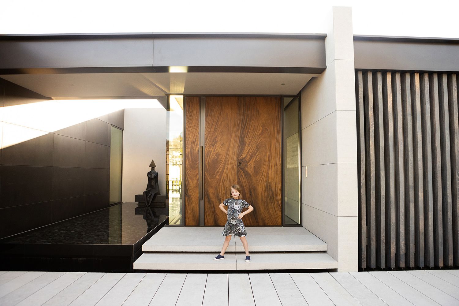 Young girl in patterned dress stands confidently in front of a modern architectural building entrance.