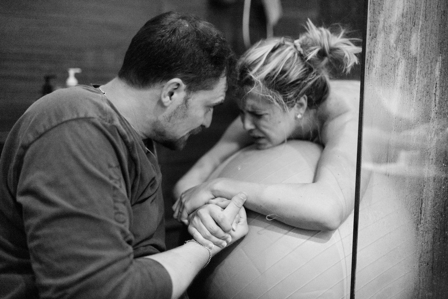 Black and white photo of a couple sharing an intimate moment, man holding pregnant womans hands during labor.