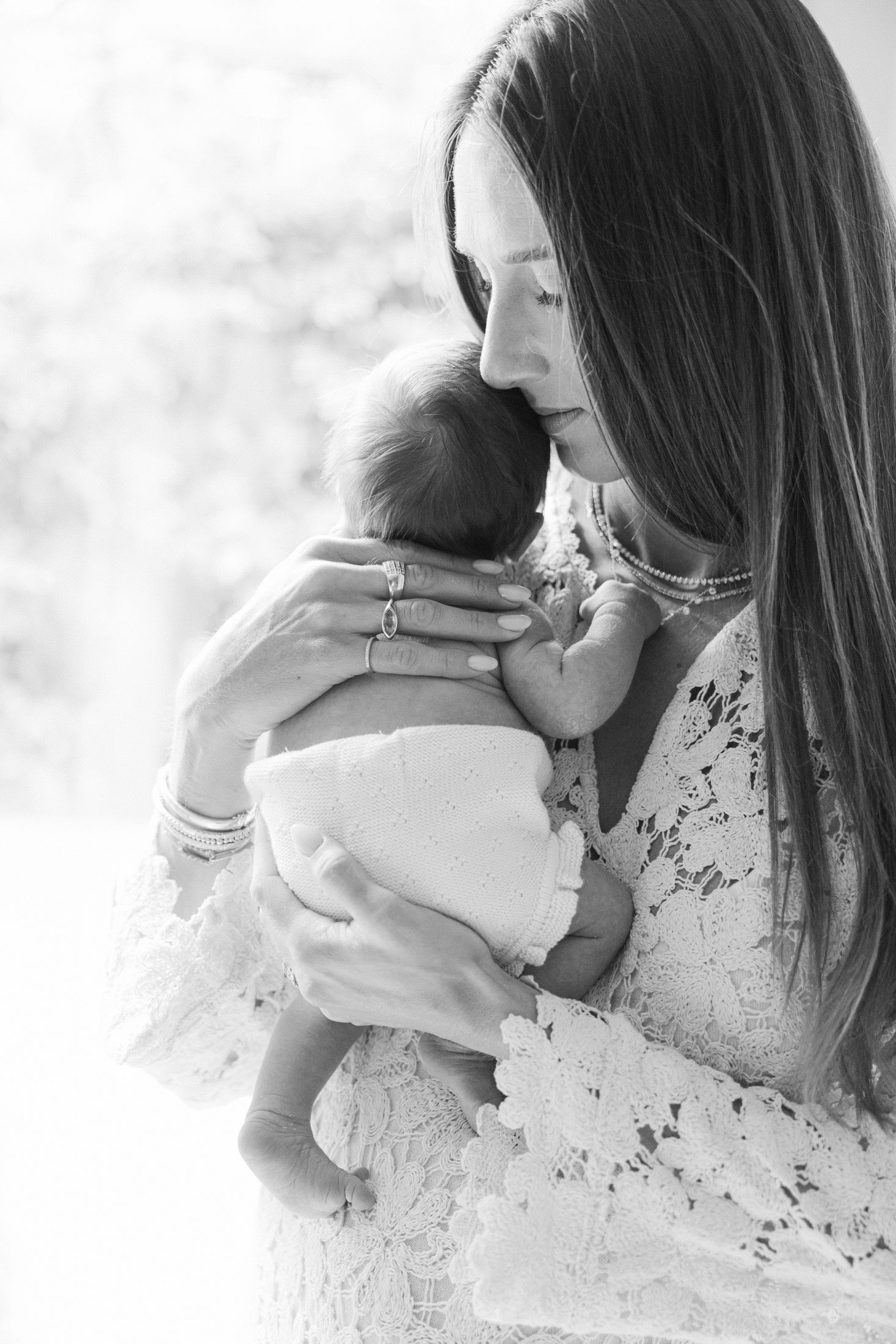 Black and white photo of a mother in lace dress tenderly holding and nuzzling her newborn baby.