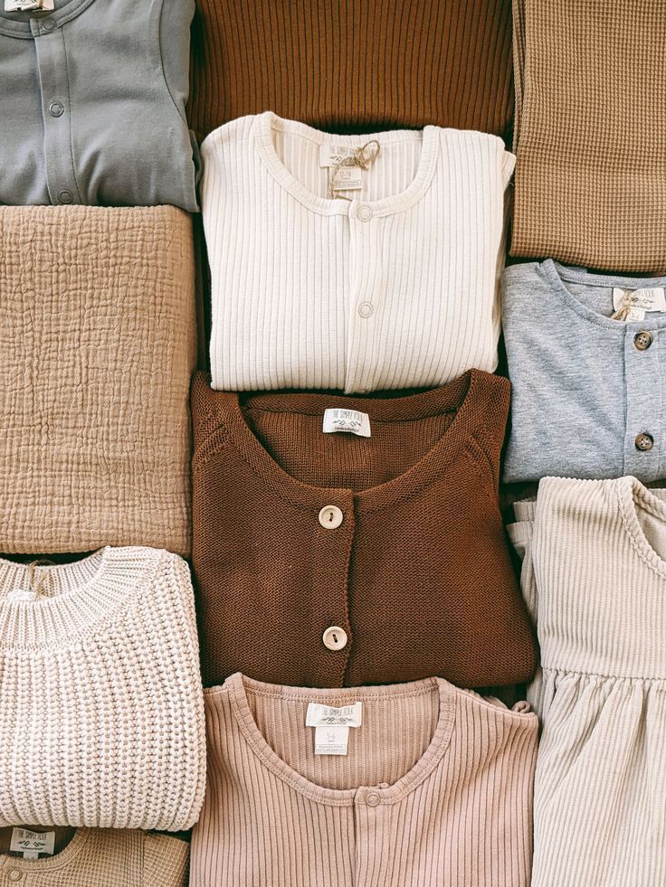 Neatly folded neutral-toned clothing items arranged in a flat lay, featuring cream, brown, blue, and beige sweaters.