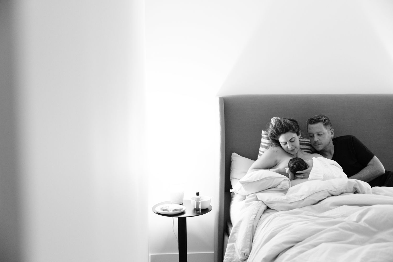 New parents rest together in bed gazing at their newborn baby after home birth delivery.
