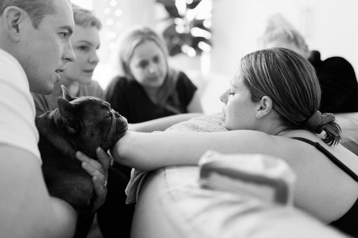 Black and white photo of a family gathered around a woman petting a small black puppy indoors.