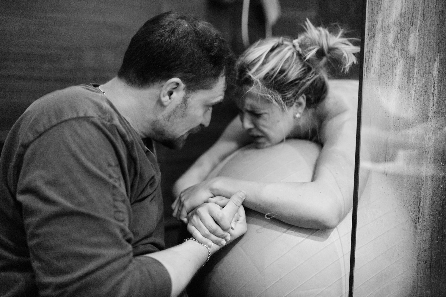 Couple holding hands intimately during water birth labor in birthing pool.