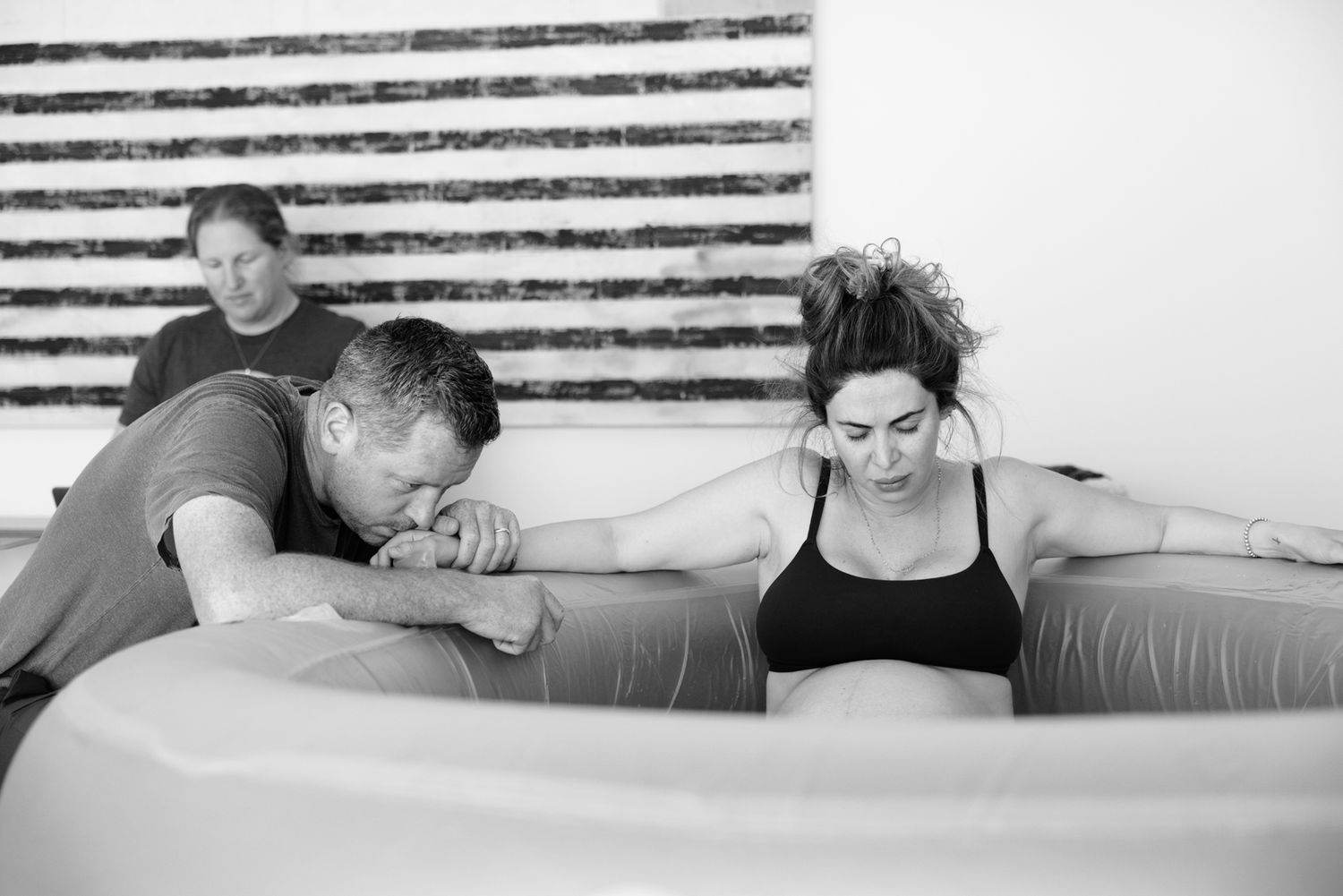 A couple and midwife support a laboring woman in a birthing pool.