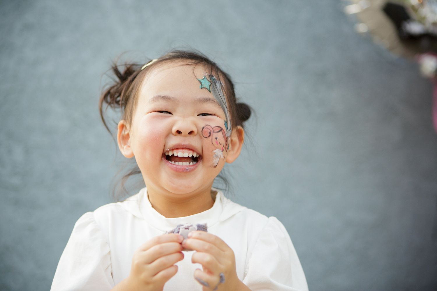 Happy little girl laughing with butterfly face paint at a birthday party celebration.