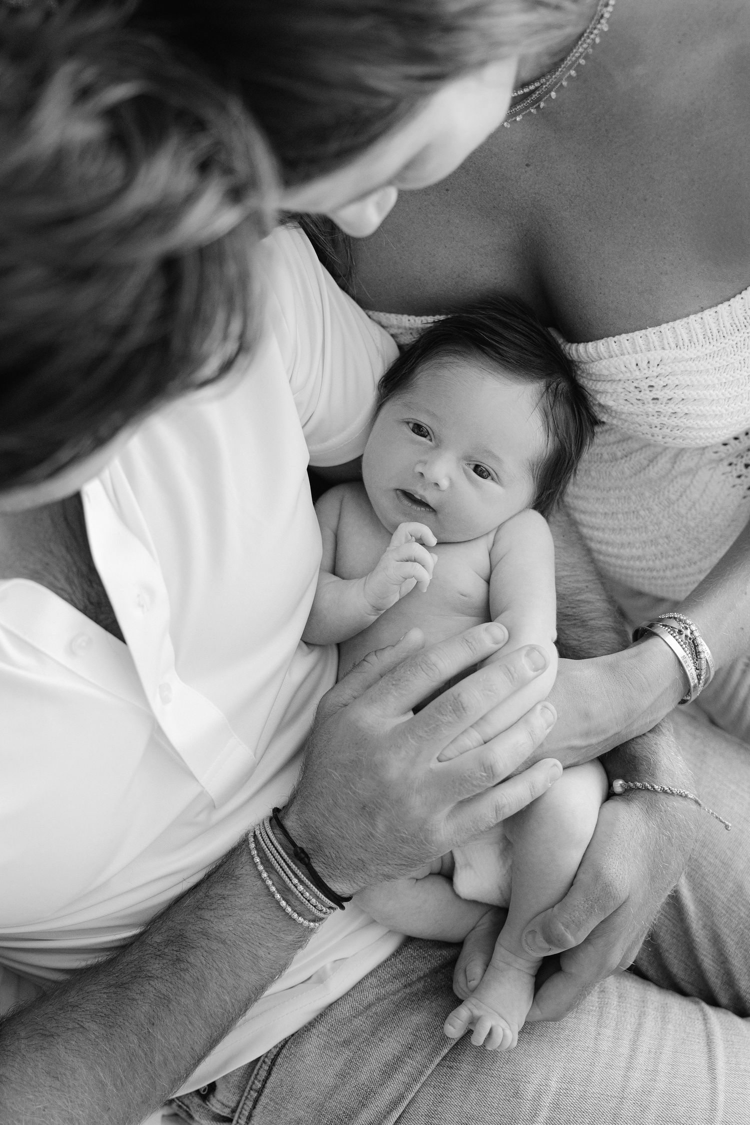 Black and white photo of parents lovingly cradling their newborn baby, capturing a tender family moment.