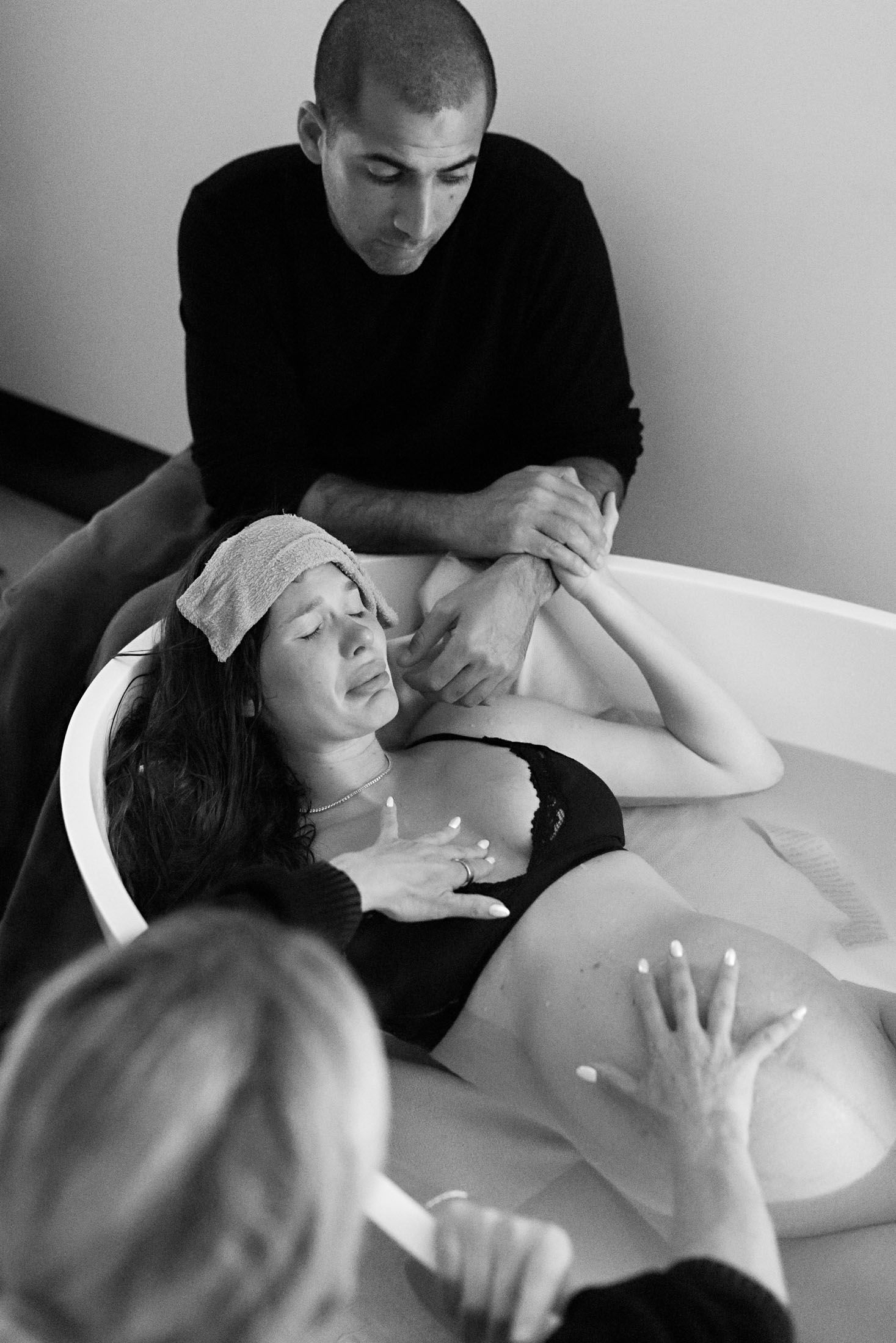 Black and white image of a woman in labor in a birthing tub, supported by her partner and midwife.