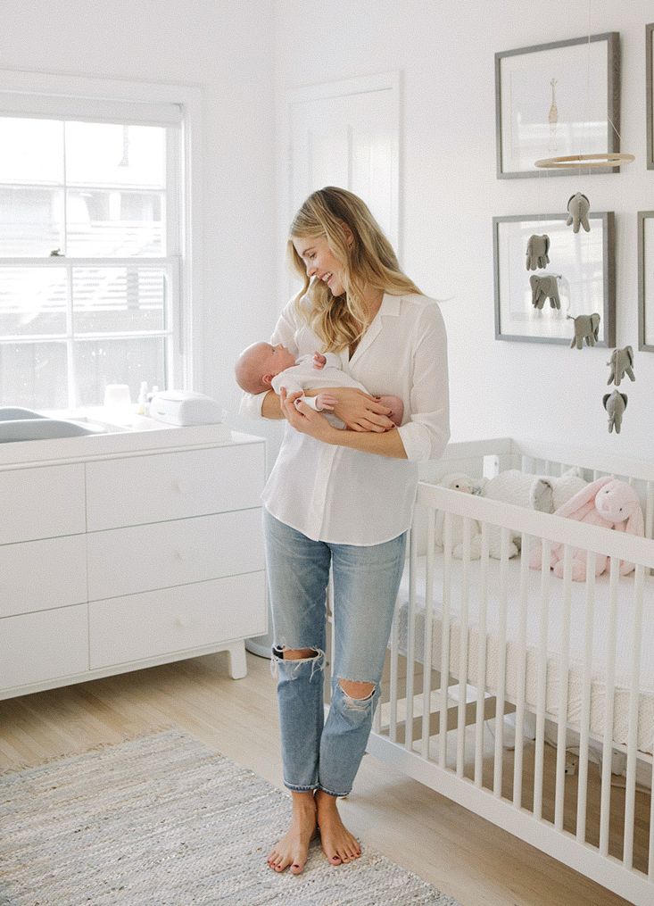 Mother holding newborn baby in bright white nursery with white crib, elephant decor, and natural light.