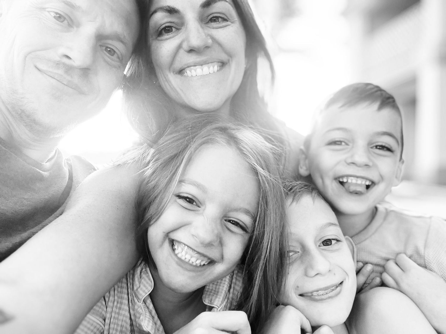 Black and white family selfie of five people smiling joyfully outdoors in sunlight.