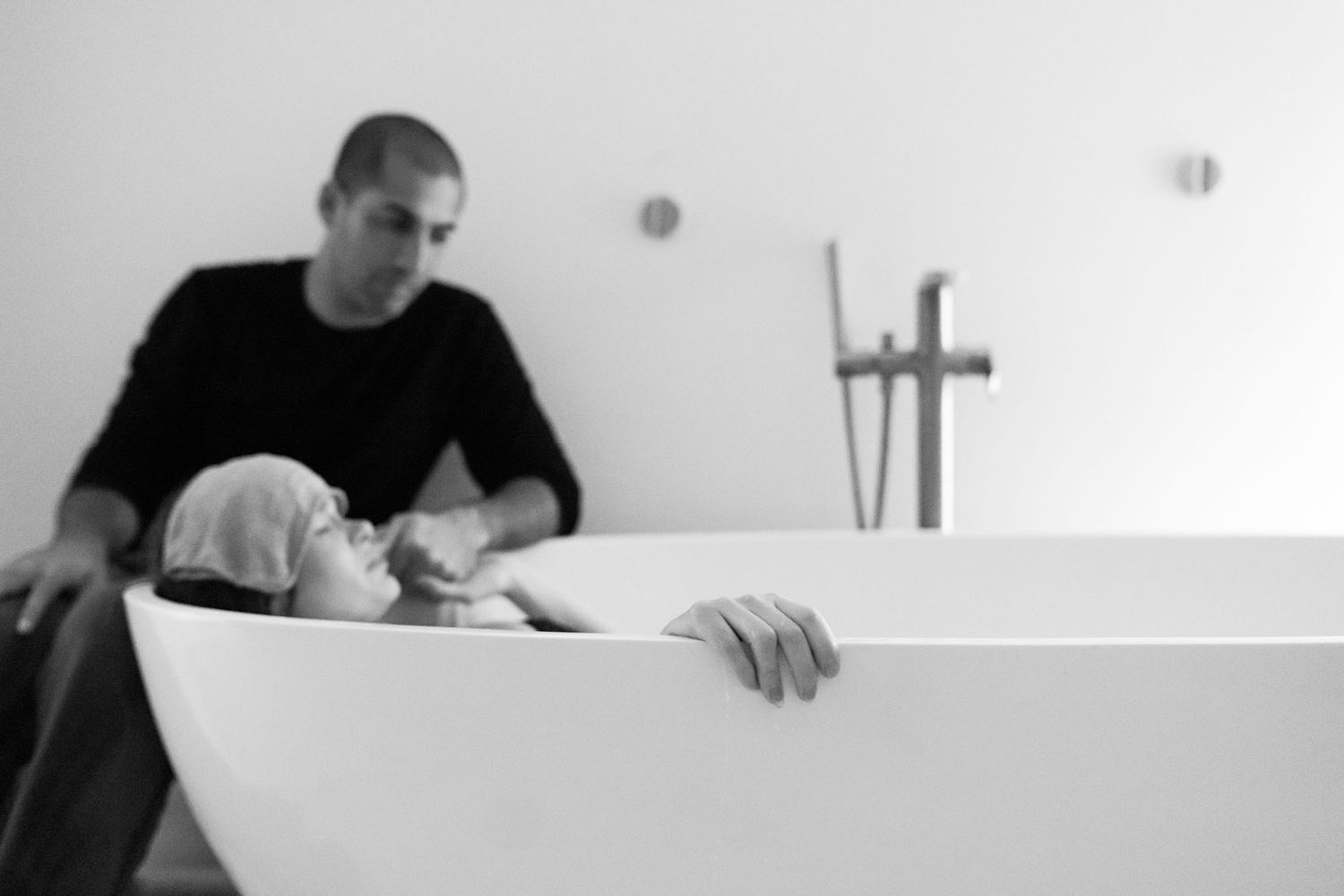 Intimate black and white photo of a man supporting a woman resting in a freestanding birthing tub.