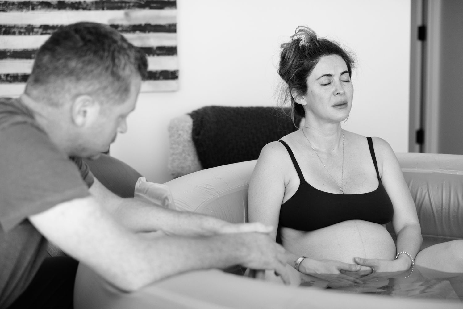 A supportive partner gently touches a pregnant womans belly as she breathes through a contraction during home labor.