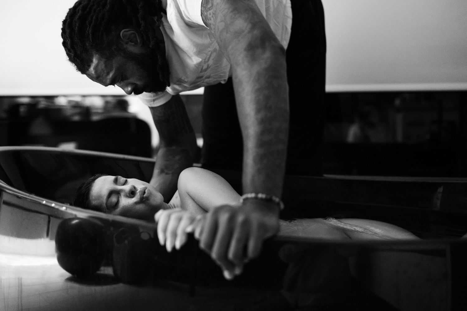 Black and white photo of man leaning over woman lying on table in dimly lit room.