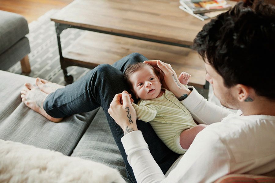 Parent cradling sleeping newborn baby on gray sofa in cozy living room with wooden coffee table.