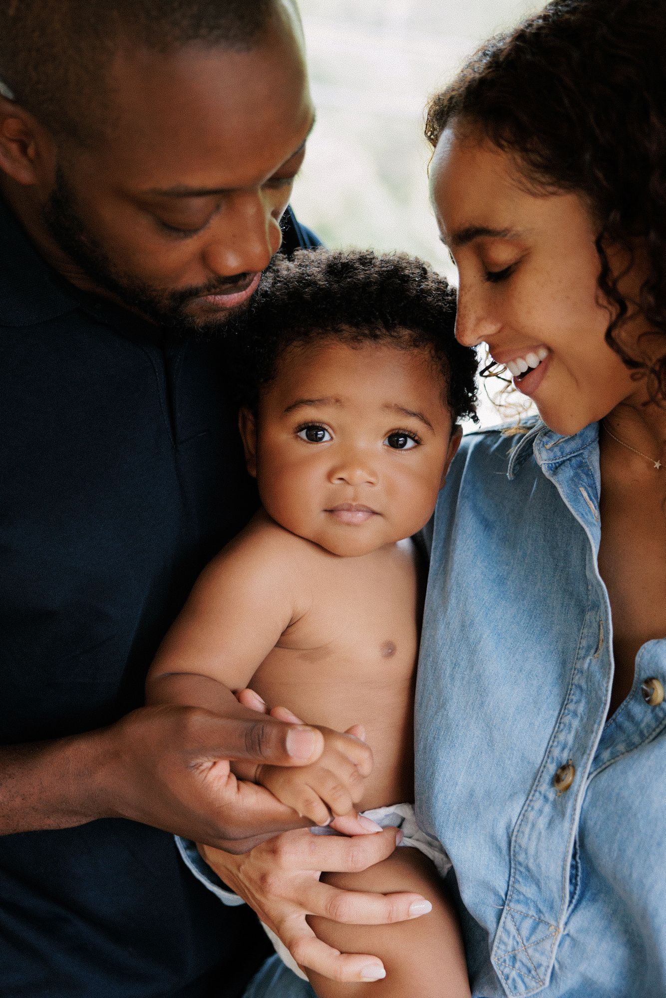 A loving family portrait of parents tenderly holding their baby, smiling warmly in a cozy, intimate setting.