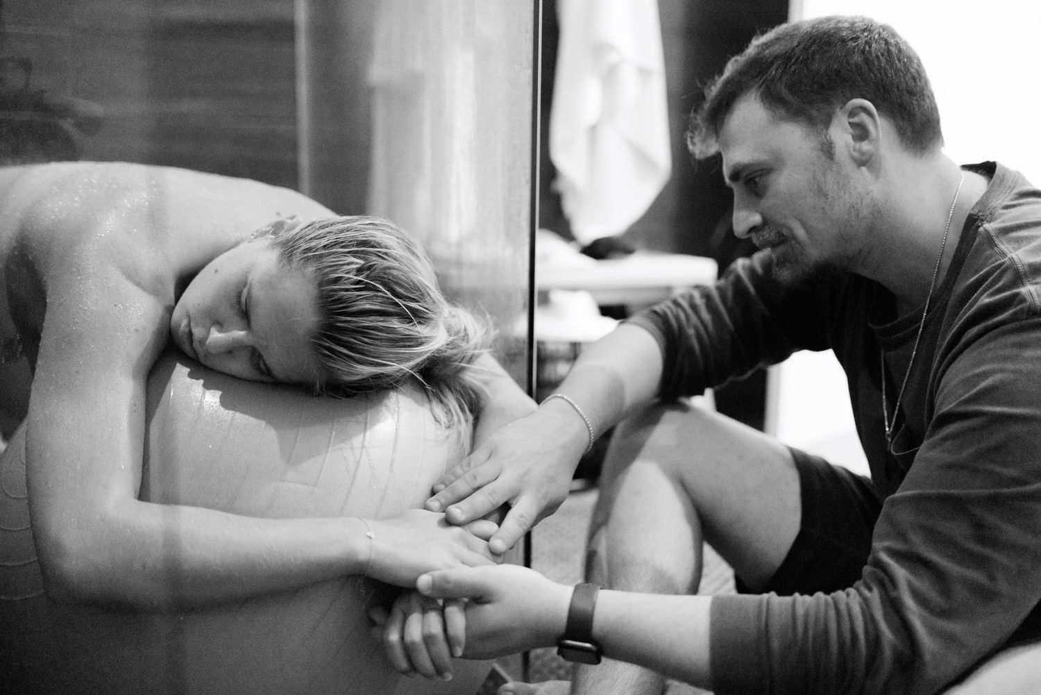 Supportive partner holding hands with laboring woman in birthing tub.