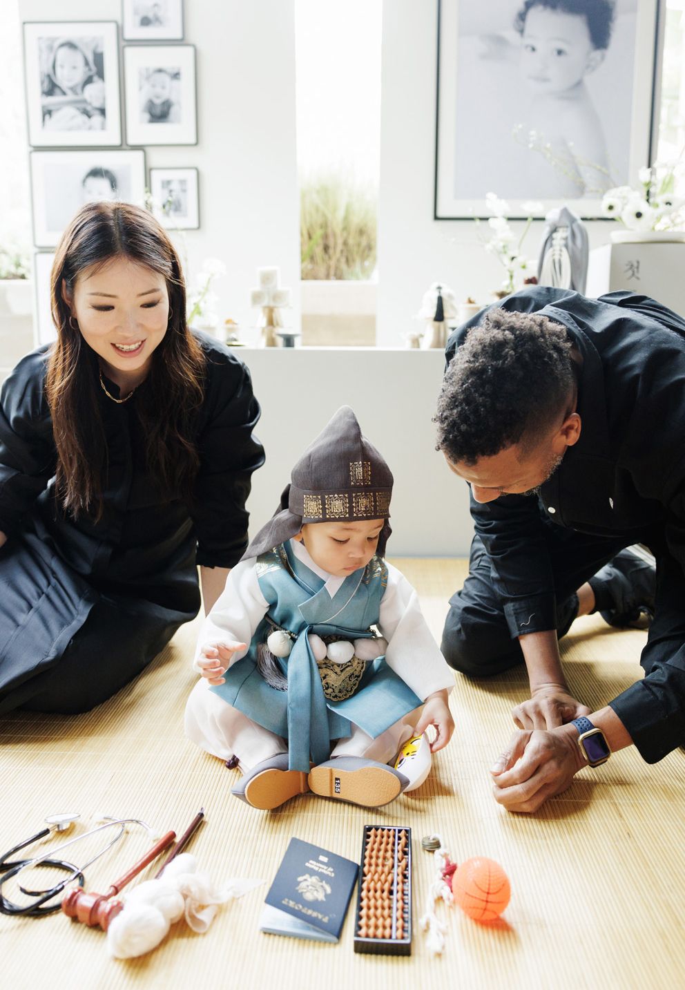 Parents in traditional Korean hanbok celebrate their baby's doljabi ceremony with symbolic objects on the floor.