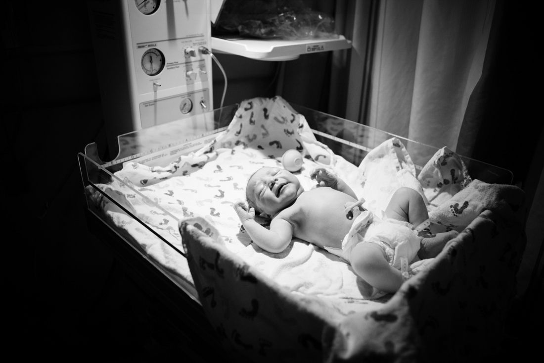 Black and white photo of two newborn babies lying in a hospital bassinet under a warming light.