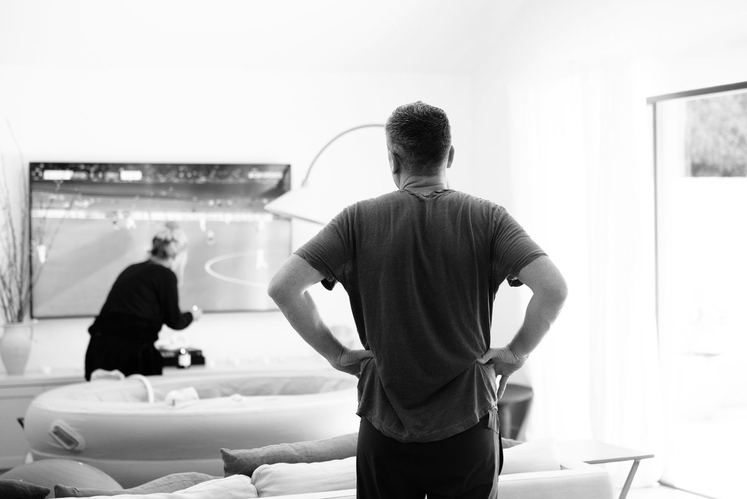 Man standing with hands on hips watching TV during partner's home labor process.
