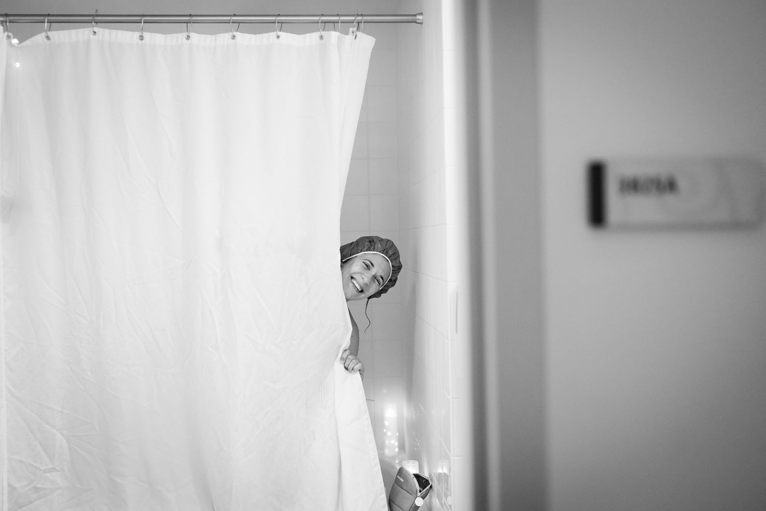 Child peeking around white shower curtain in black and white bathroom photo.