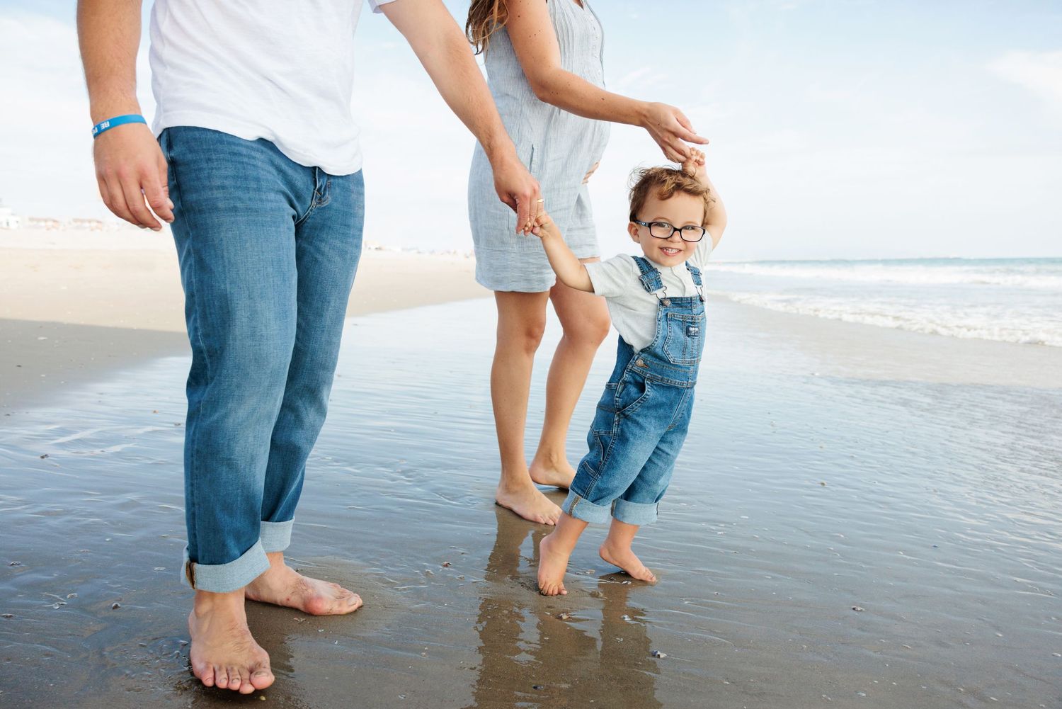 Family of three walking barefoot together on a wet sandy beach by the ocean.