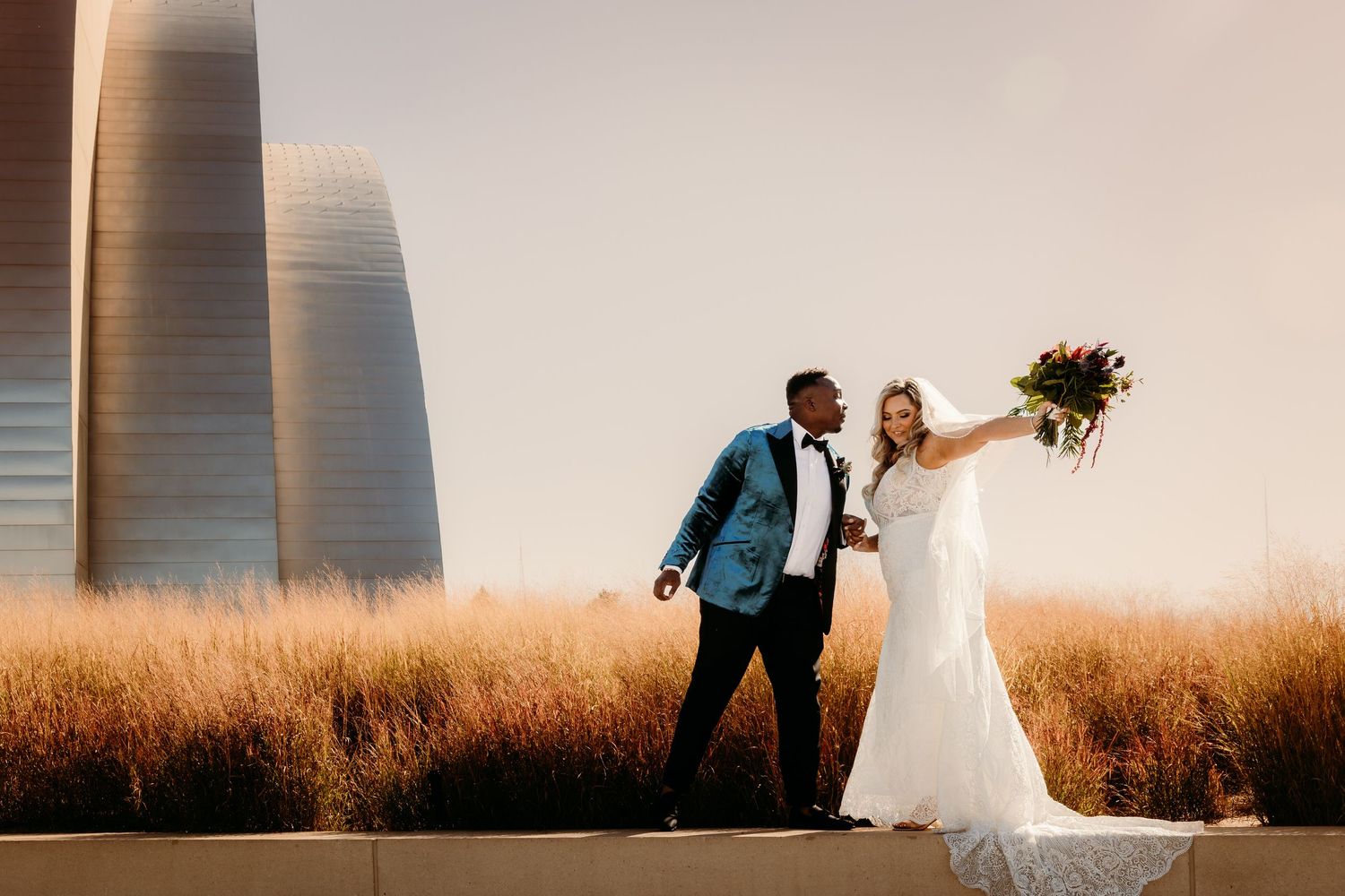 Wedding couple posing dramatically against modern architecture at golden hour.