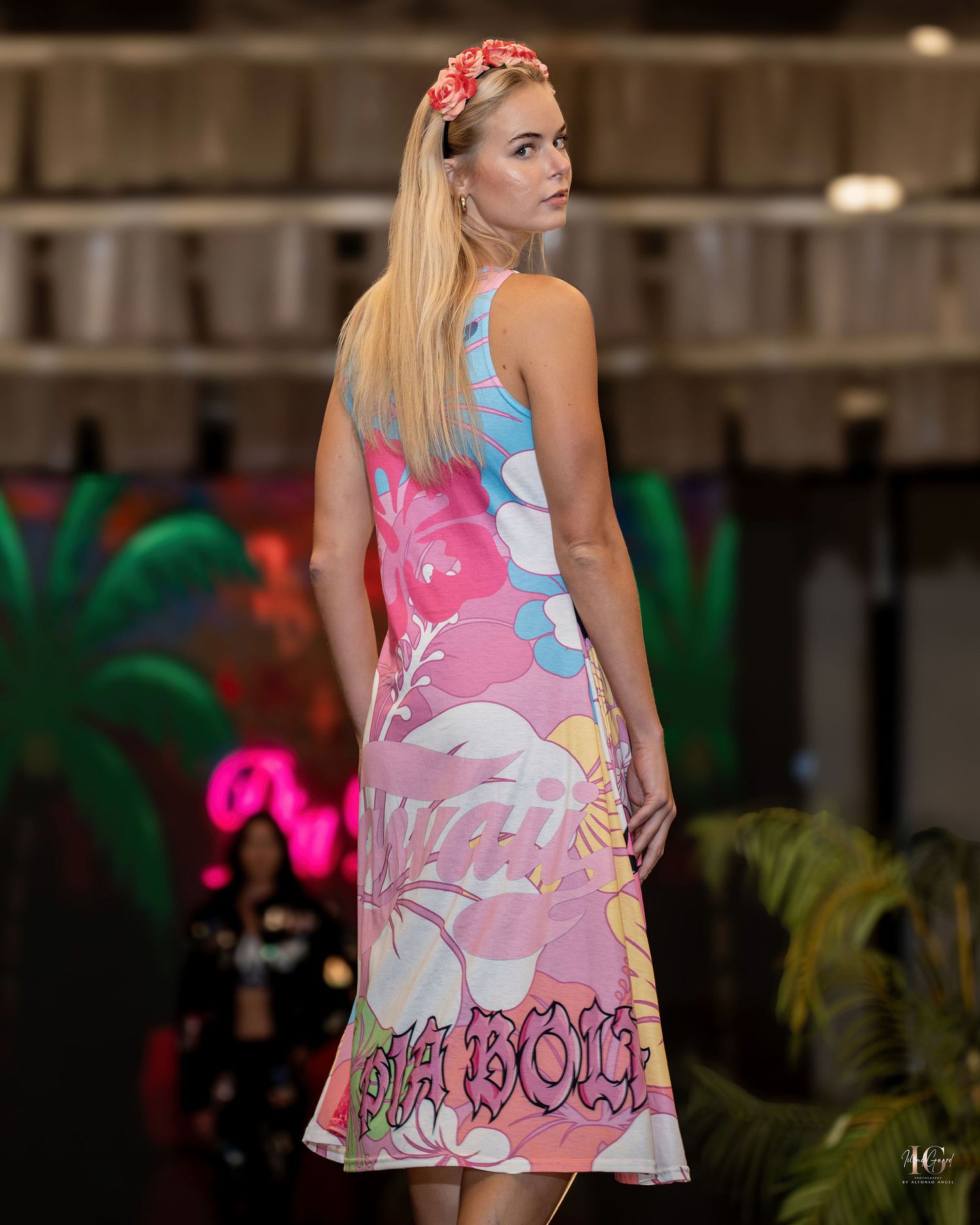 A model walks the runway in a floral print swing dress with pink and blue tones during a fashion show.