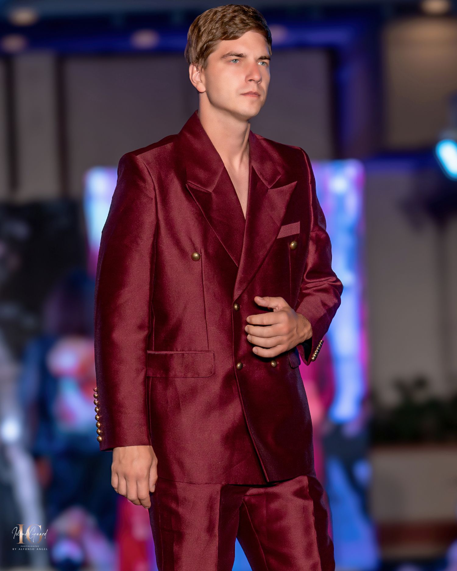 Burgundy silk formal suit displayed on fashion runway with dramatic lighting.