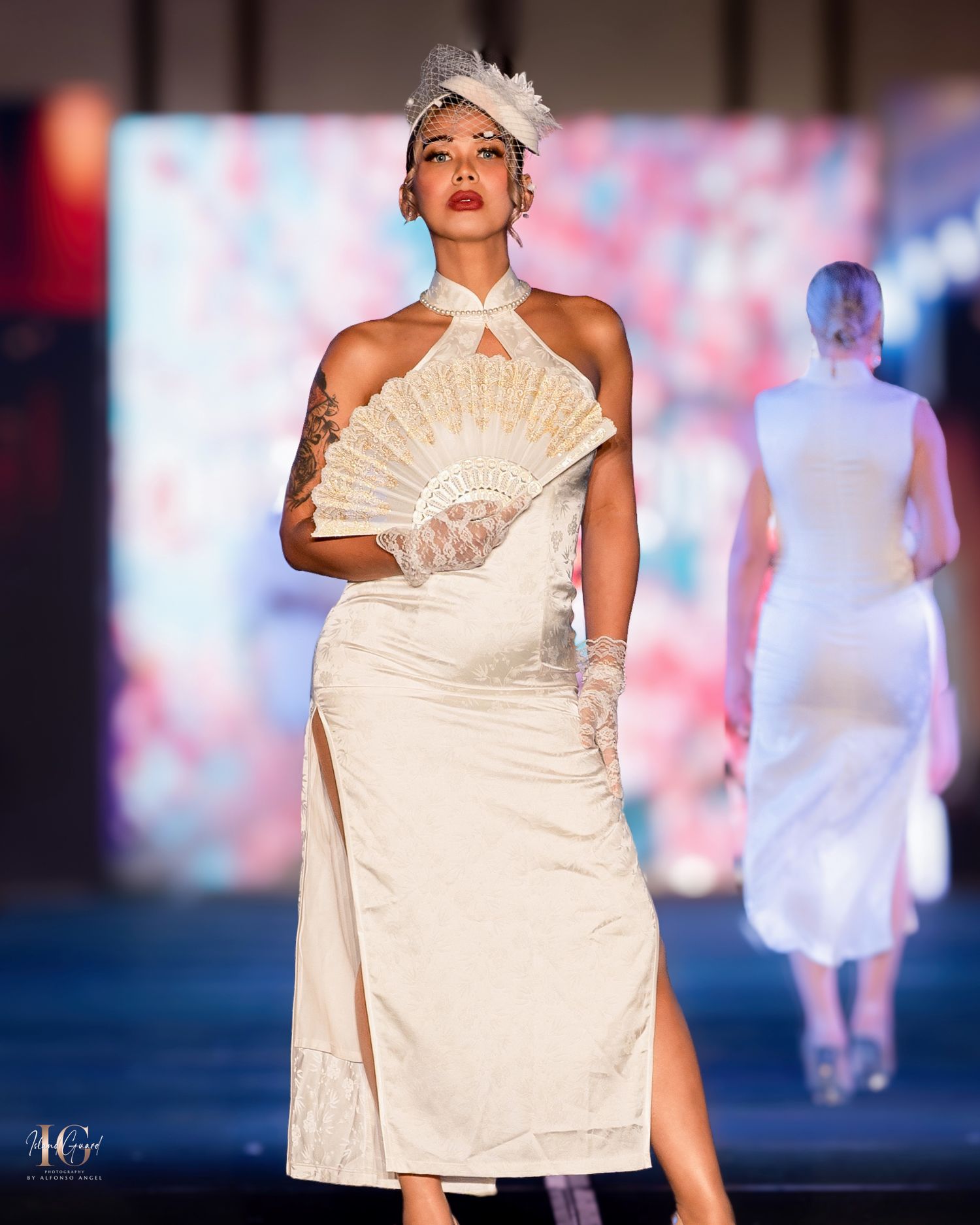 Model presents white structured dress with decorative fan detail on fashion runway.