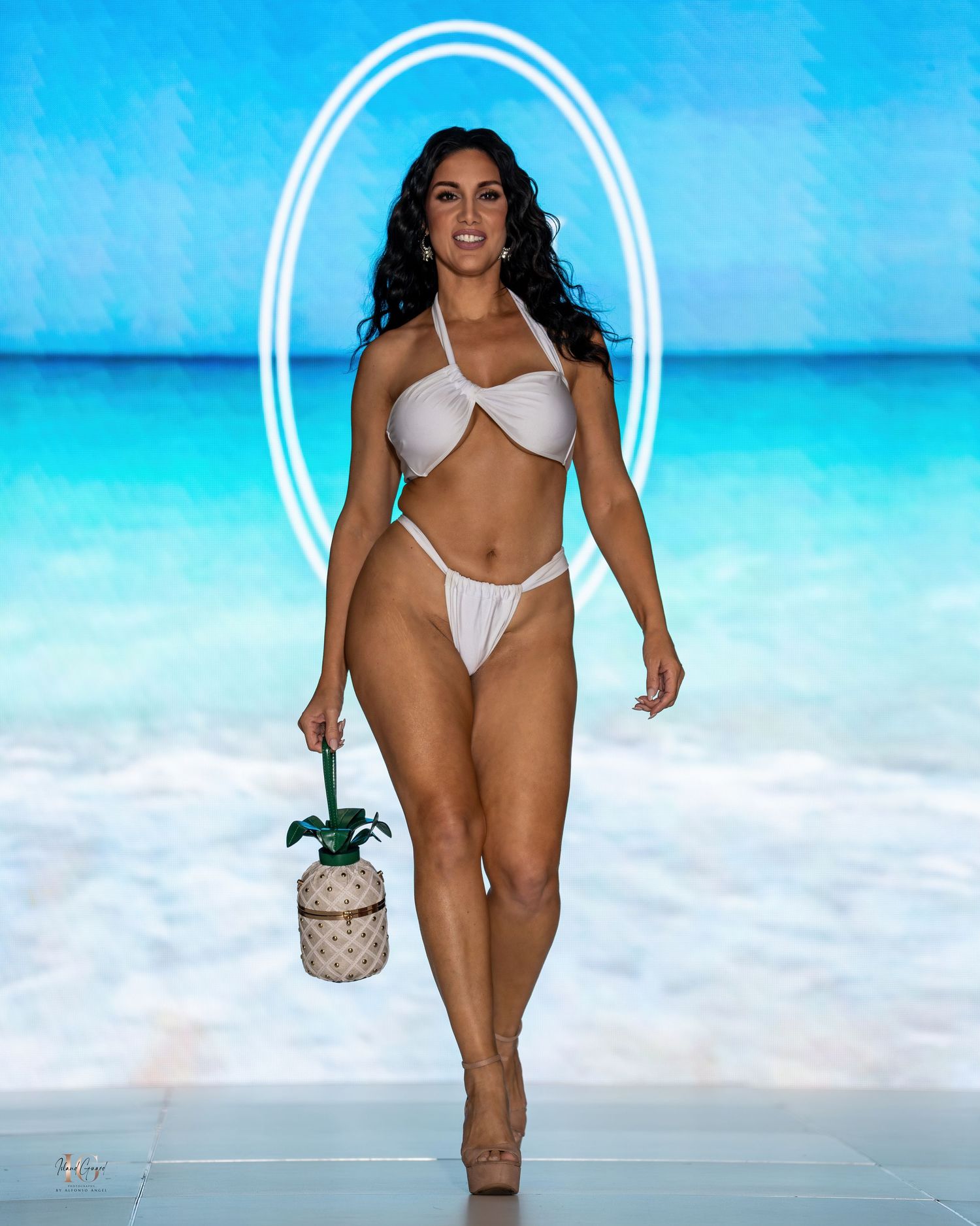 Models showcase white swimwear and accessories on runway with beach background.