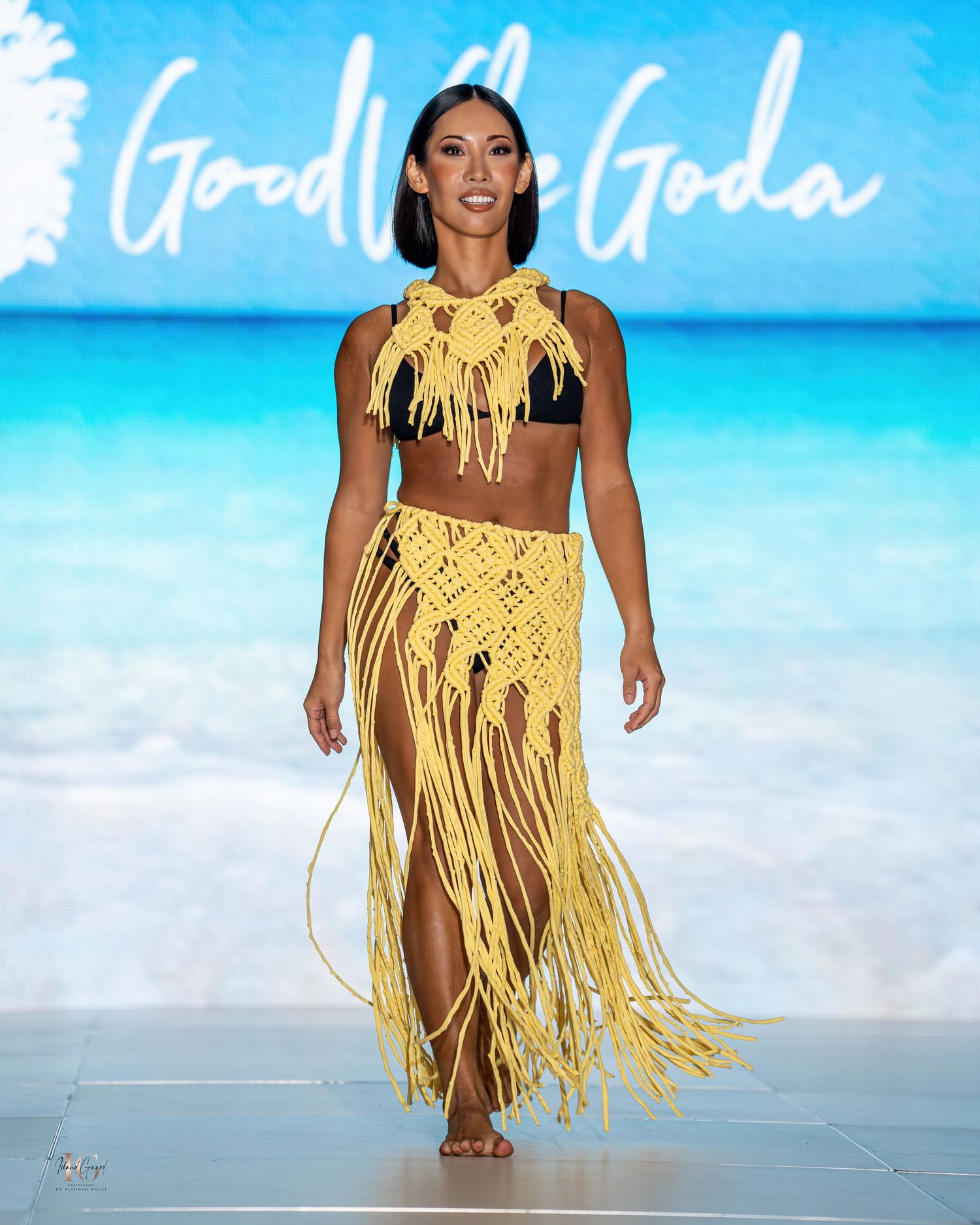 Yellow fringe two-piece swimwear ensemble with macrame details presented on tropical runway.