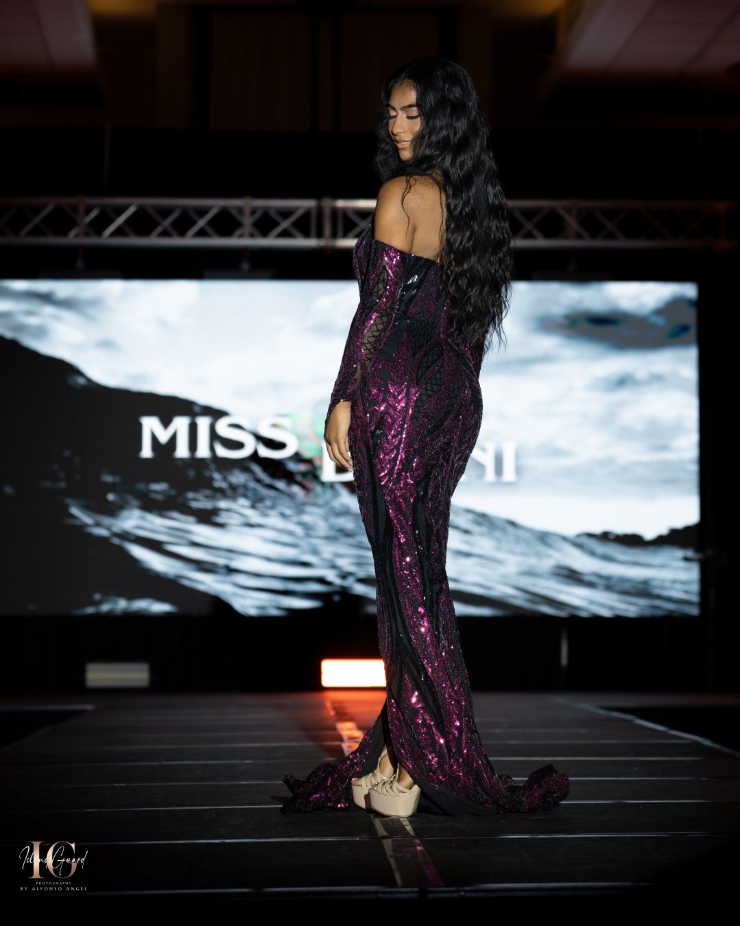 Model walks the runway in a stunning purple sequined evening gown at a beauty pageant fashion show.