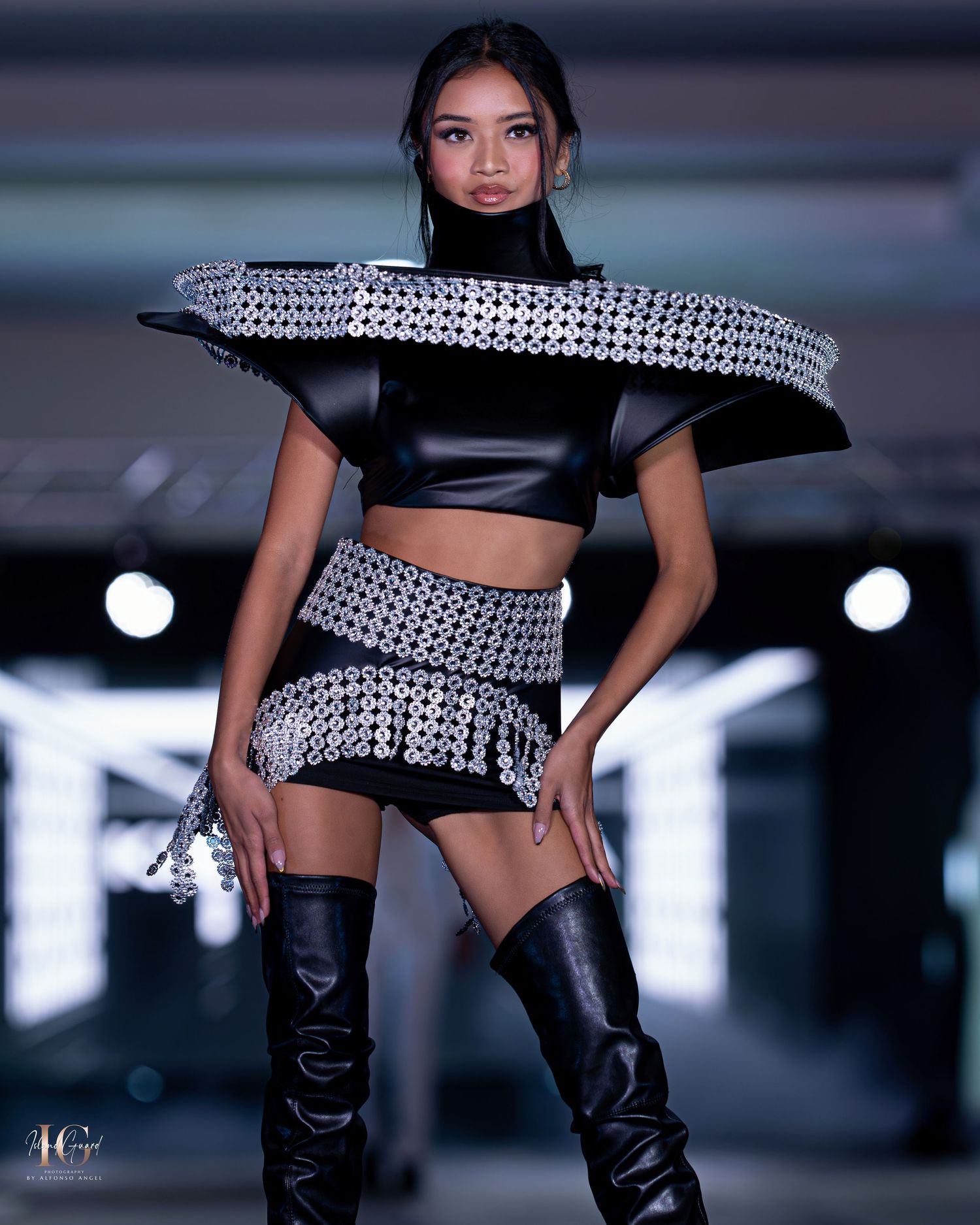 Modern fashion look featuring black crop top, patterned skirt and tall boots on illuminated catwalk.