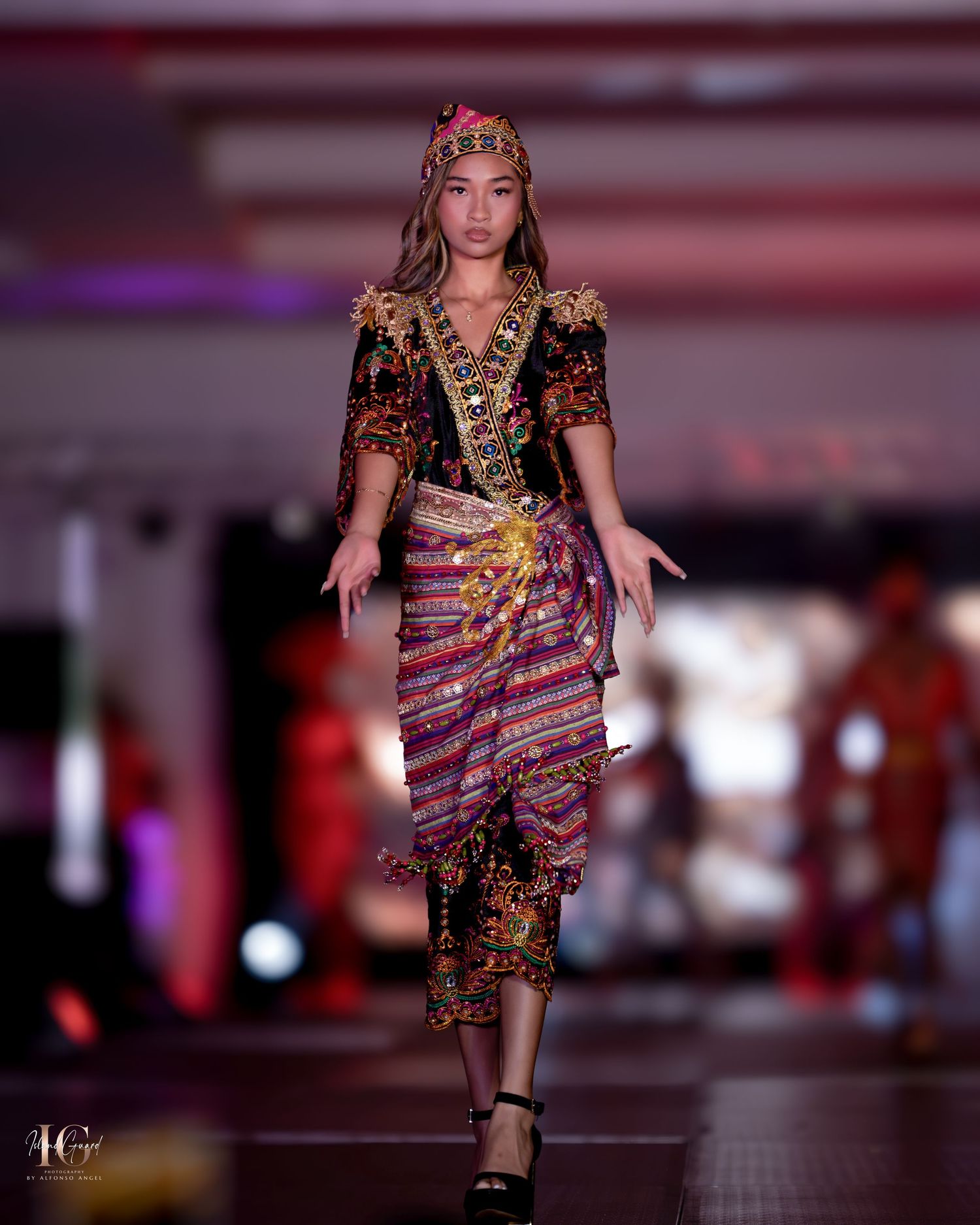 Model in traditional Asian-inspired outfit with patterned wrap skirt and ornate headpiece.