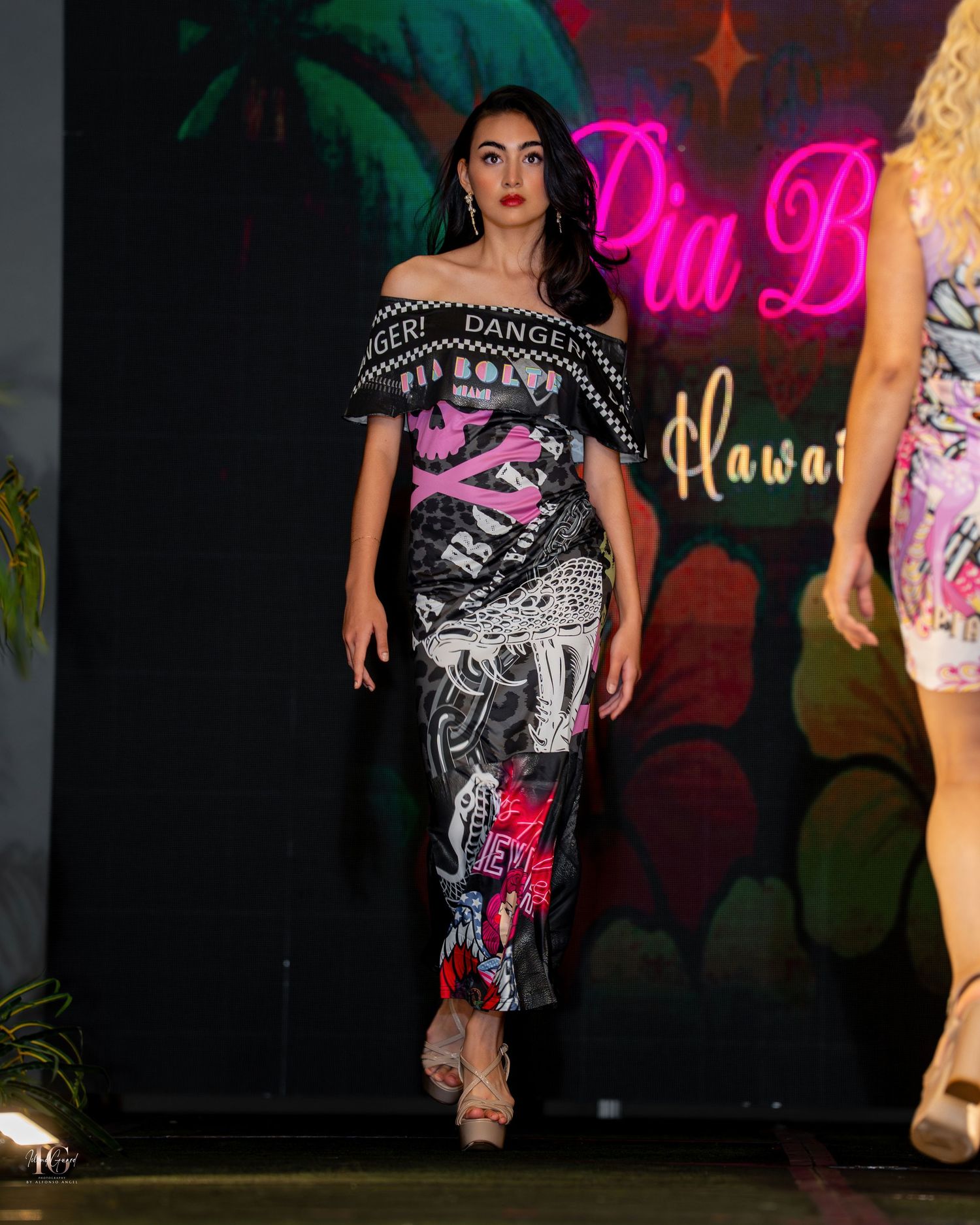 A performer in black and white graphic clothing strikes a dynamic pose on a dark stage with neon lighting.