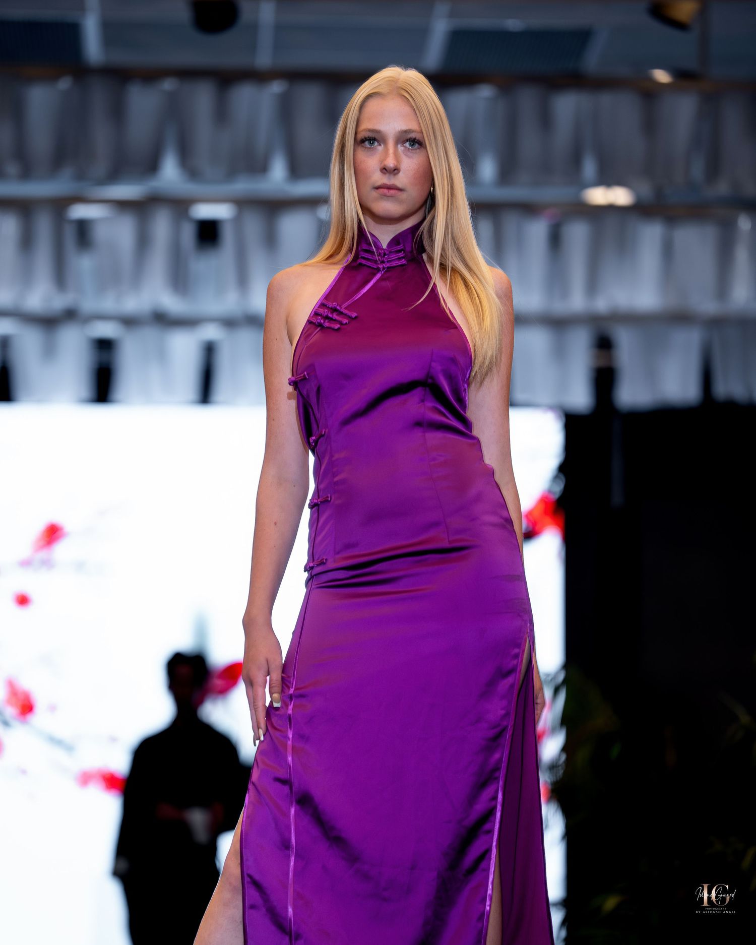Model walks runway in vibrant purple satin evening gown during fashion show presentation.