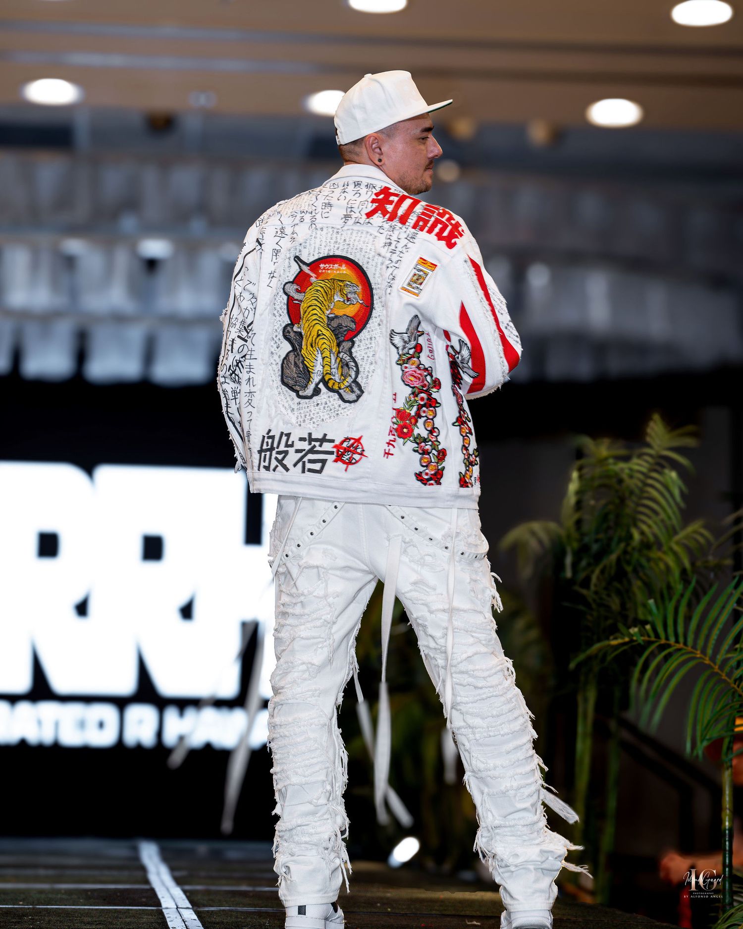 White denim jacket with colorful embroidered designs and patches displayed from multiple angles on a hanger.