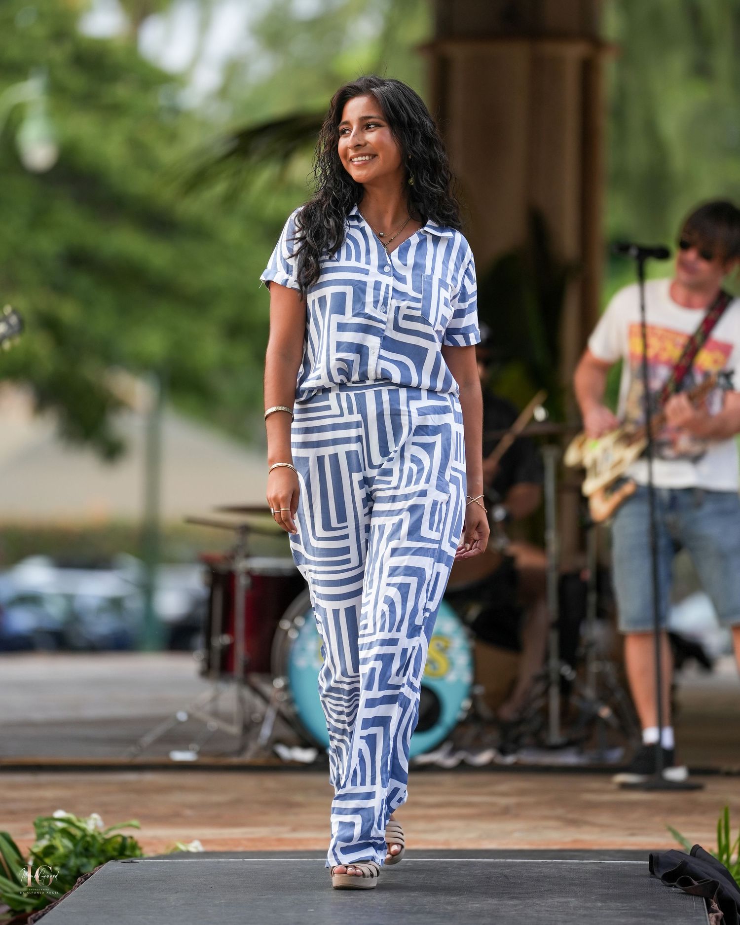 A dancer in a blue and white patterned dress performs gracefully on an outdoor stage during a summer event.