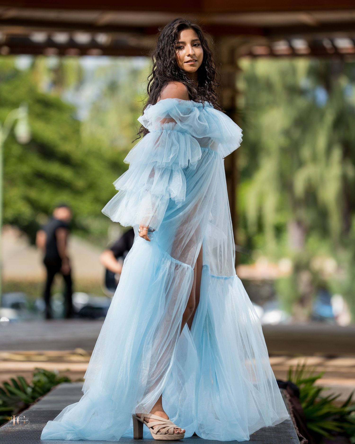 A flowing light blue tulle dress with ruffles creates an ethereal silhouette against a garden backdrop.