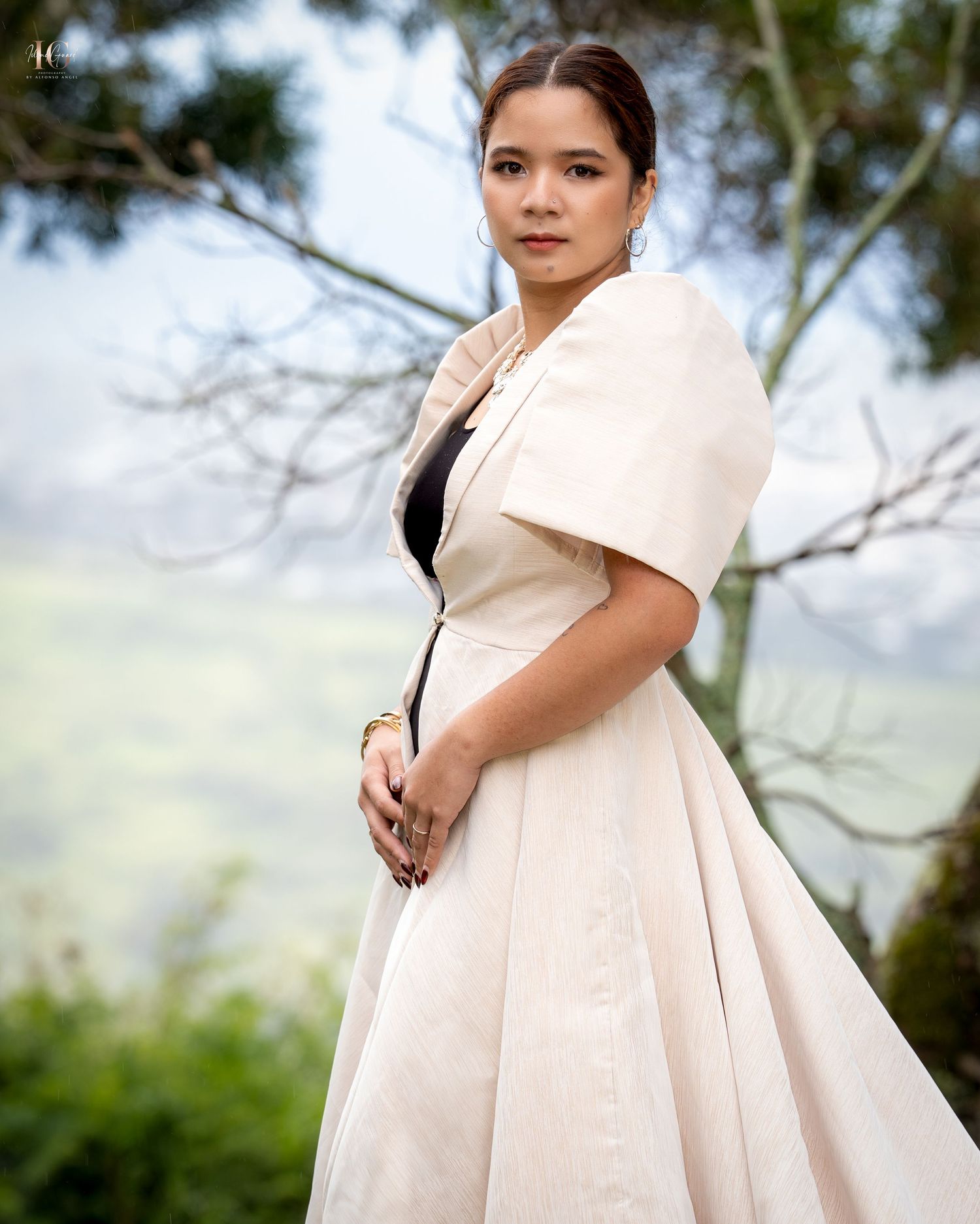 Person wearing an elegant cream colored dress with dramatic pleats and off-shoulder design in an outdoor setting.
