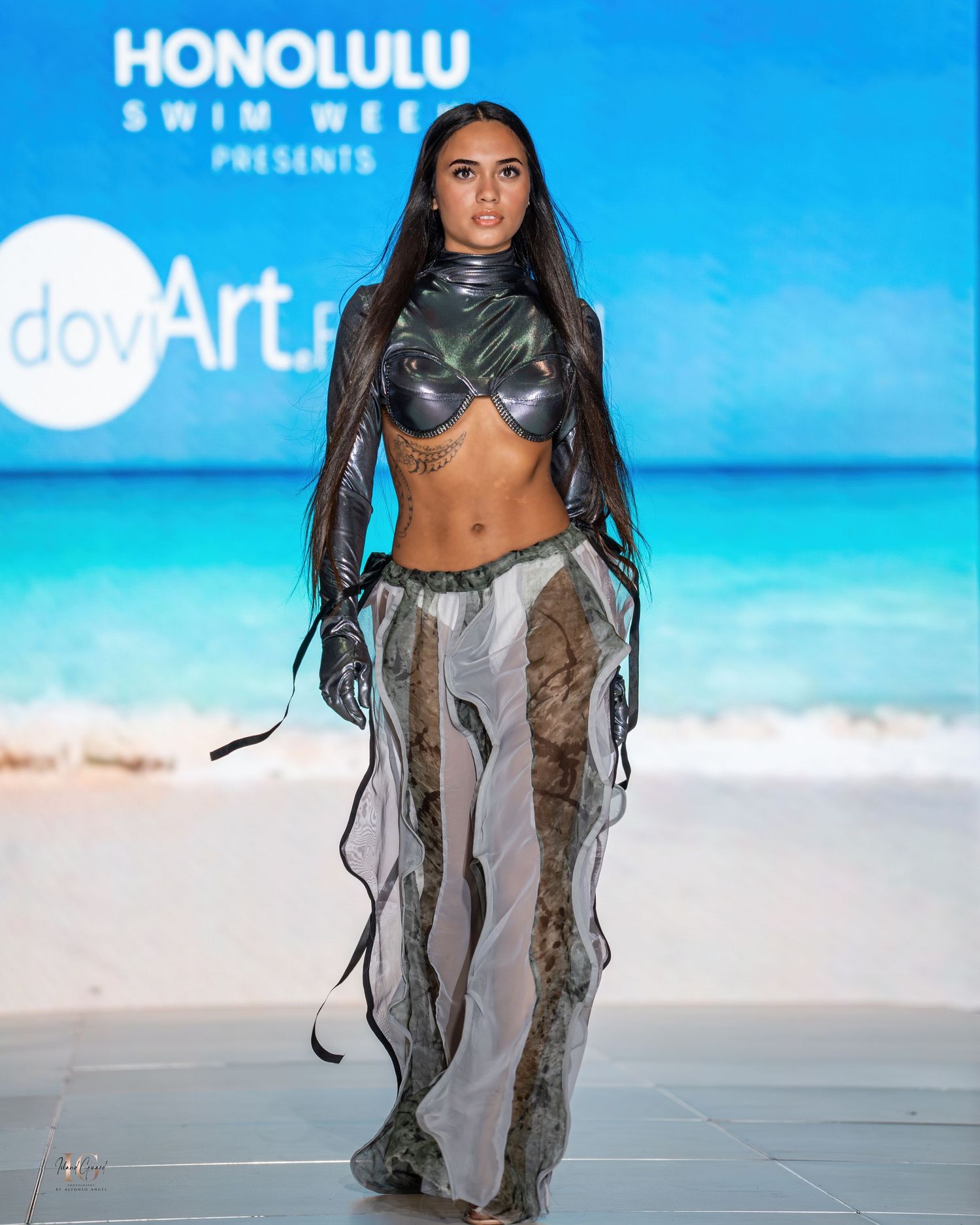 Edgy resort wear featuring metallic details and sheer panels presented on beachside runway.
