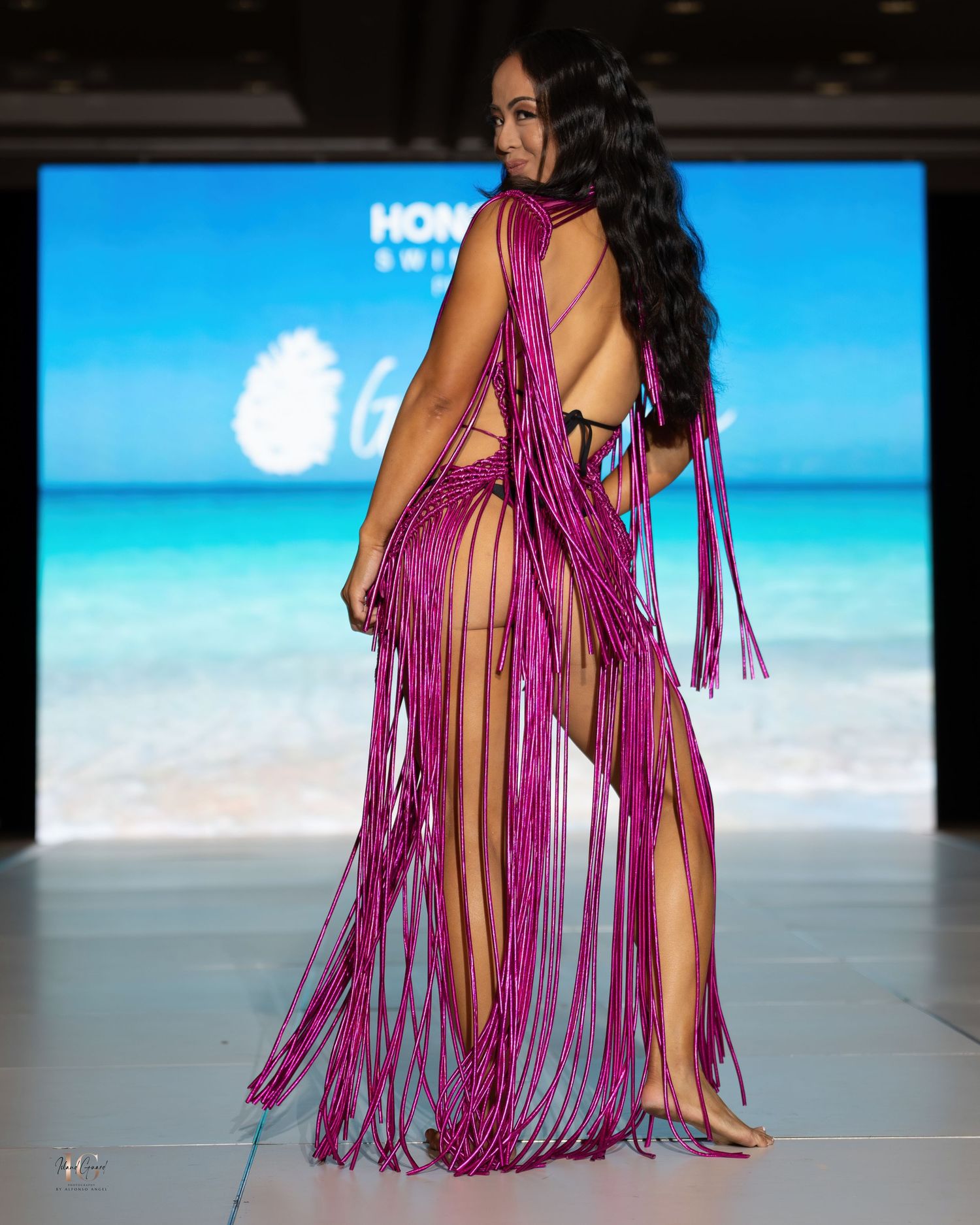 Fuchsia fringe swimwear ensemble with dramatic side slits shown from back angle on runway.