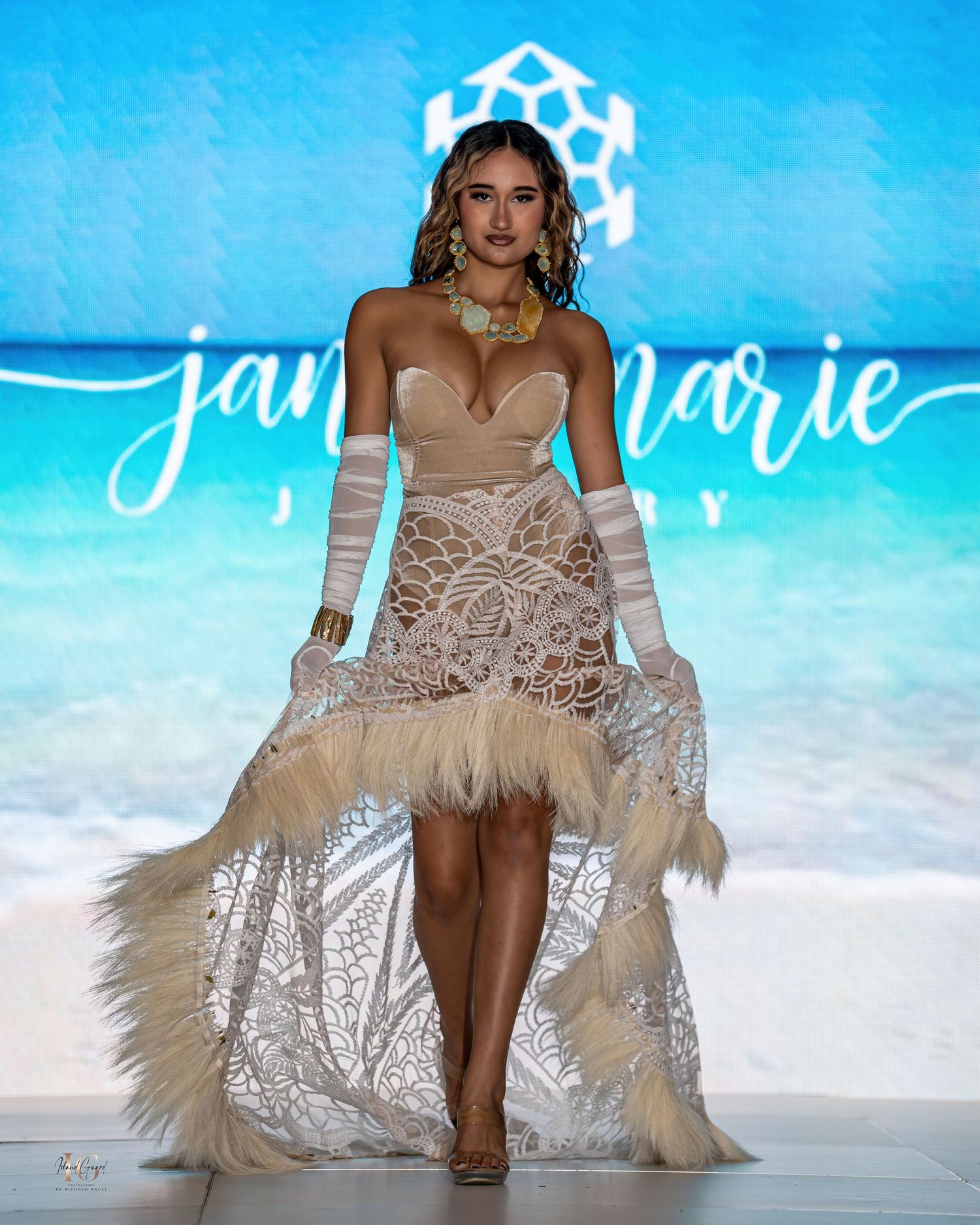 Model walks runway in embellished white feathered swimwear during beach-themed fashion show.