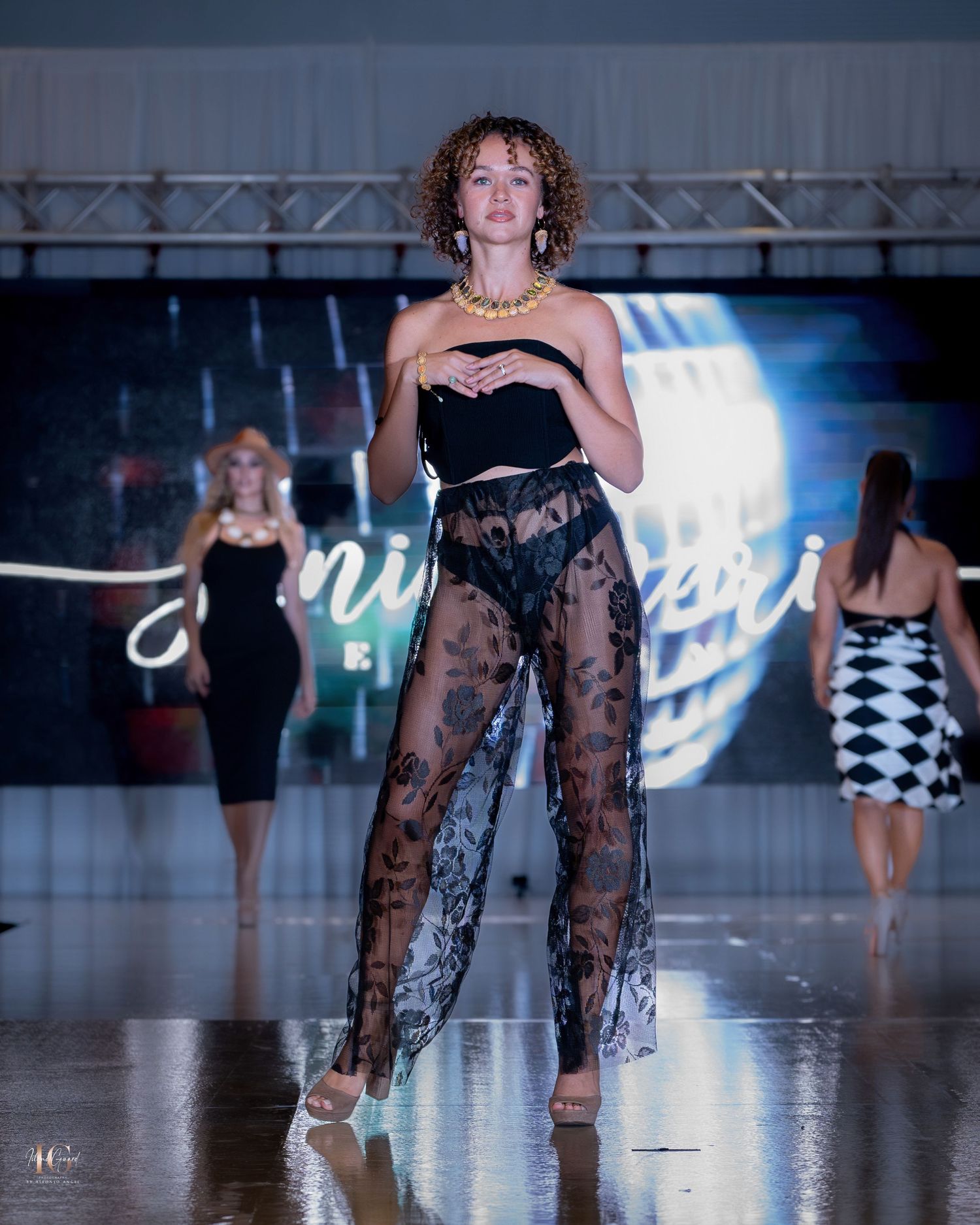 Model in black lace pants and crop top walks runway at fashion show.