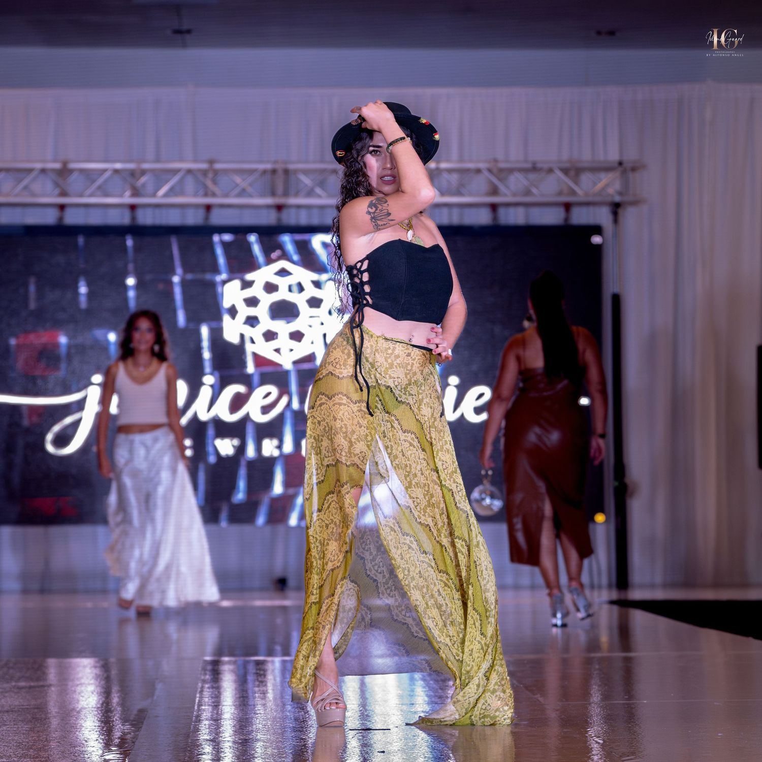 Model walks runway in flowing gold evening gown with dramatic side slit at fashion show.