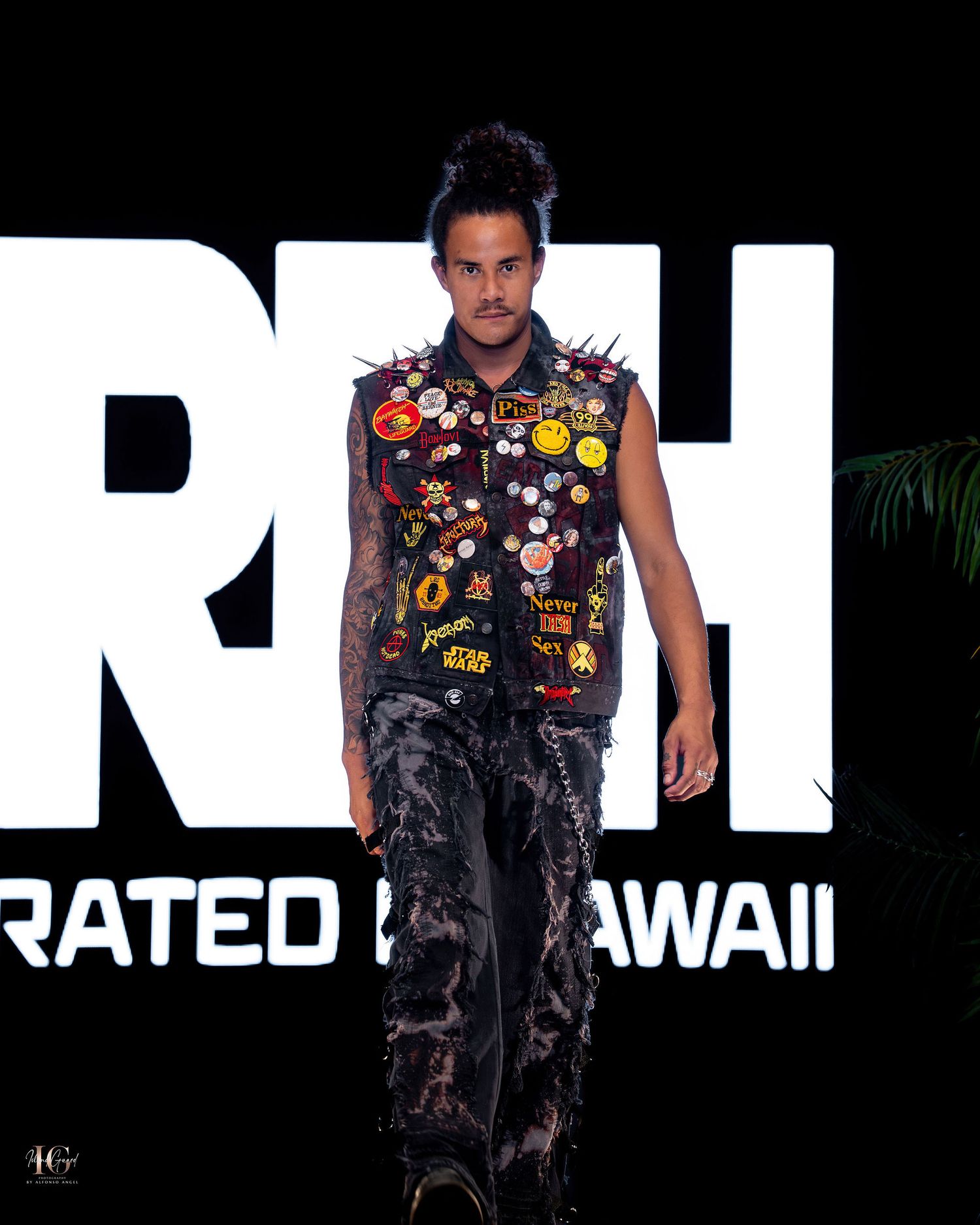 A person wearing a colorful cartoon-printed sleeveless shirt and distressed pants poses against a dark background with large text.