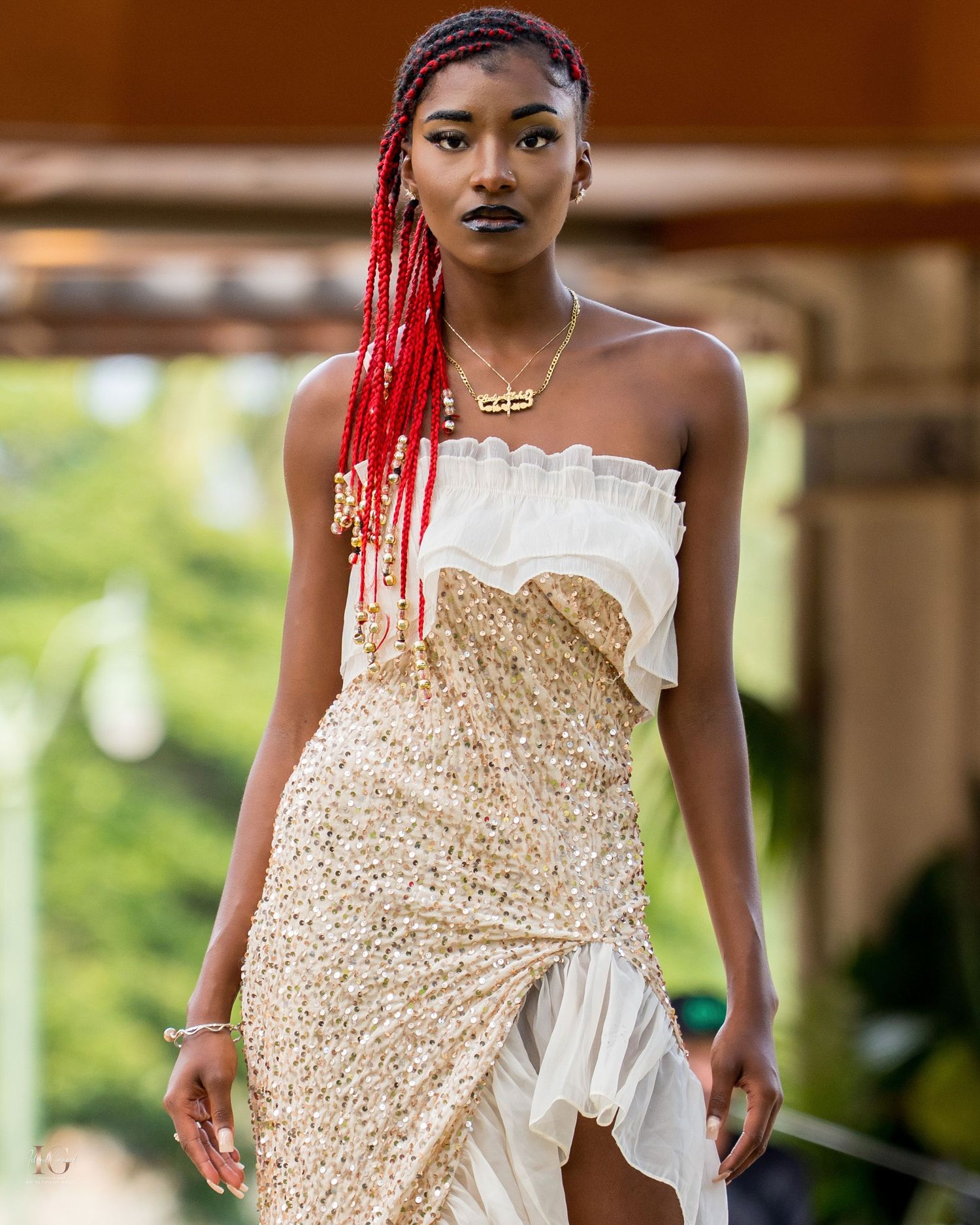 Fashion model wearing a dramatic gold sequined and white asymmetrical dress with red beaded hair accessories.