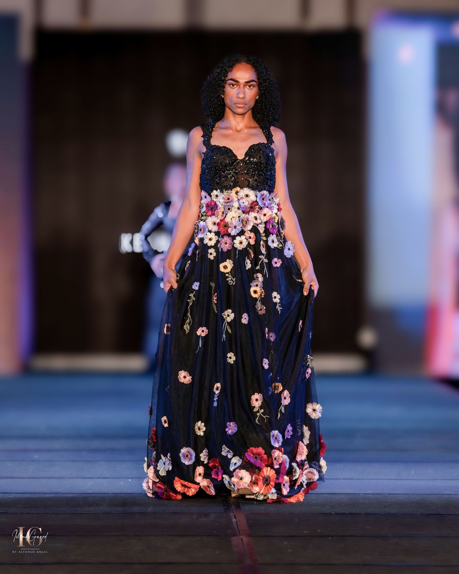 Navy blue dress with colorful floral print and full skirt presented at fashion show.
